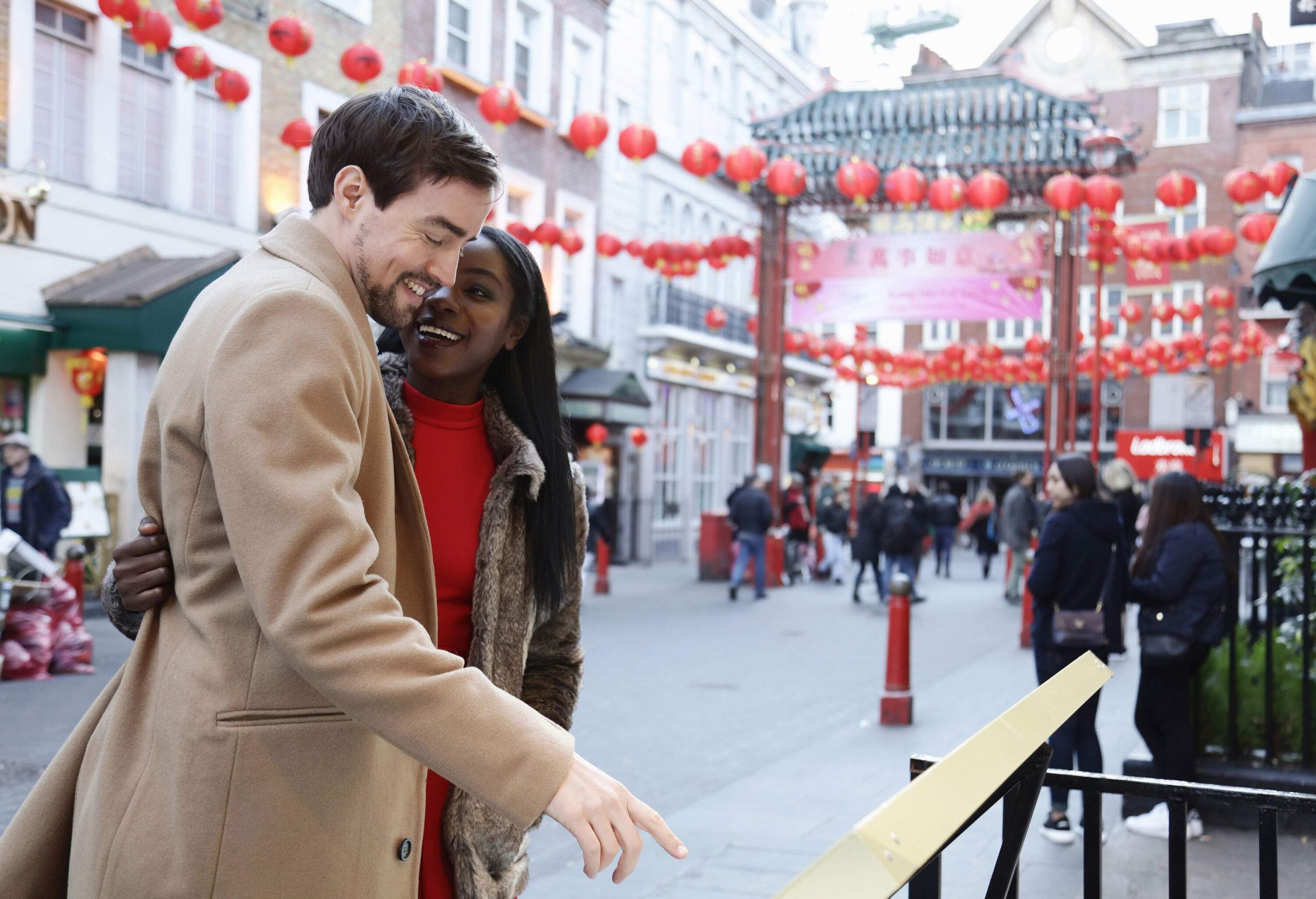 A young couple along a square decorated with red ball lanterns surrounded by tall buildings.