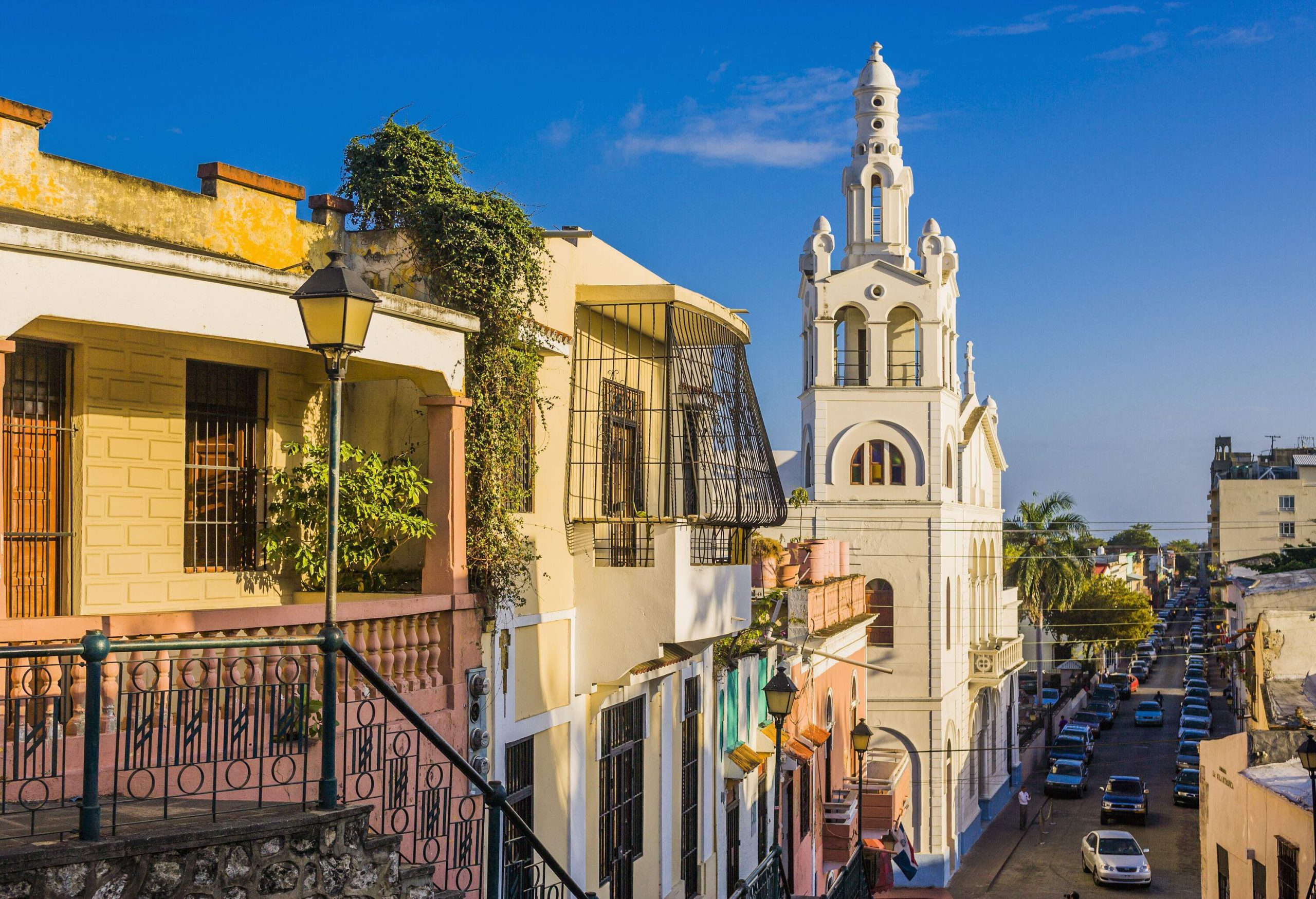 A white church looming over a city street crowded with parked cars.