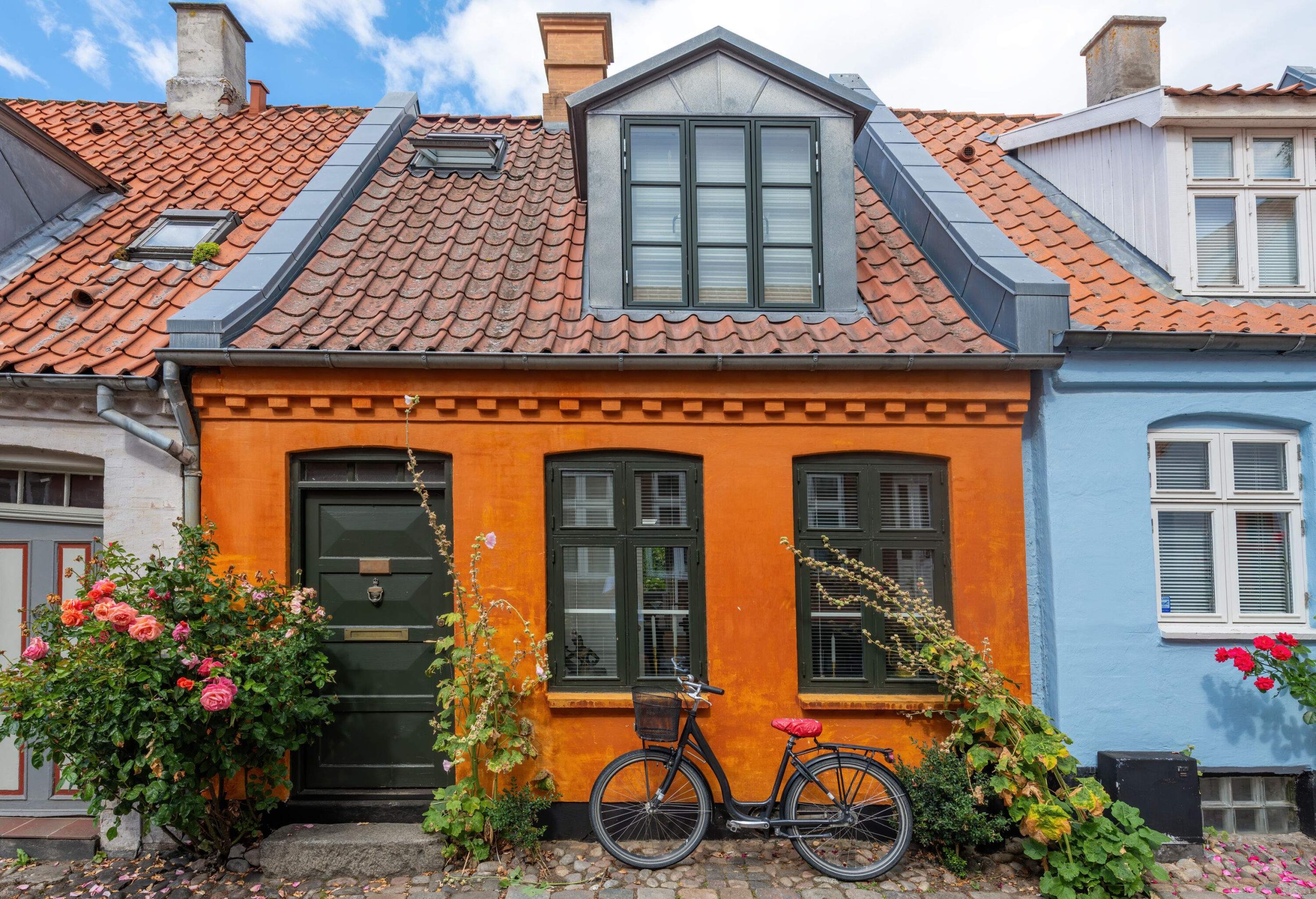 A bicycle leaning against the window of an orange cottage.