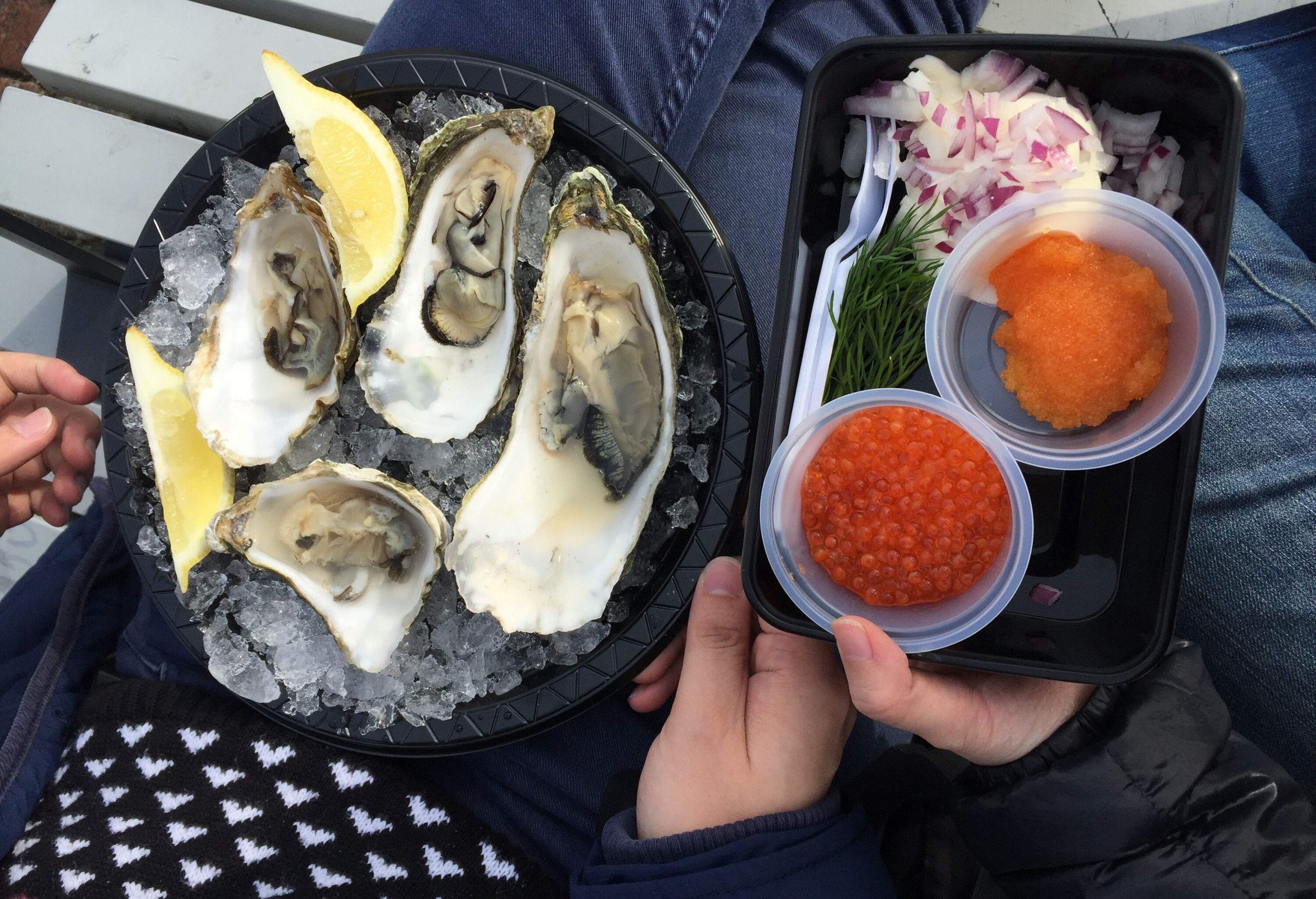 A bowl of crushed ice with fresh oysters and a platter of dipping sauce and minced onions.