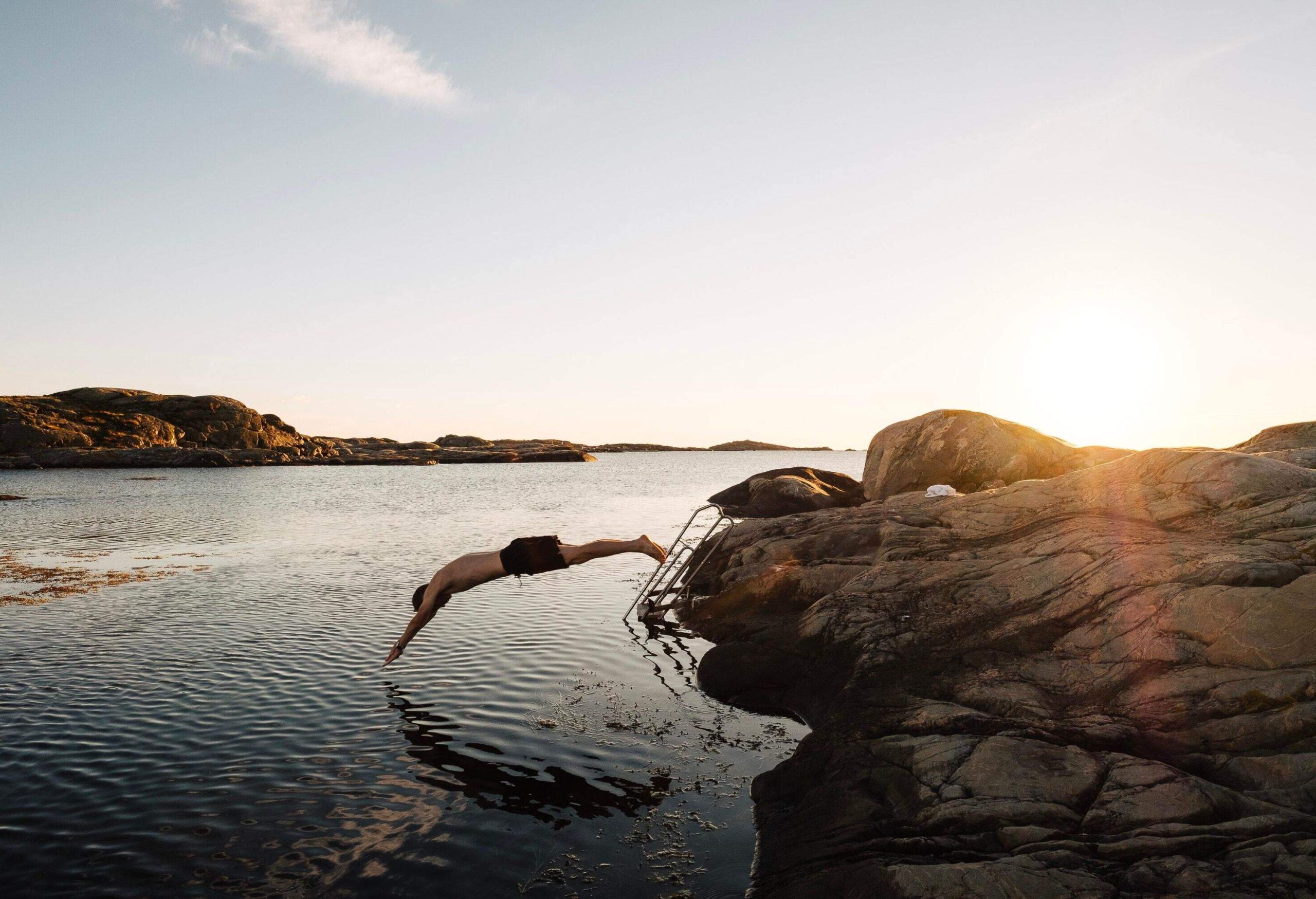 A man in swimming trunks dives into the ocean from a coastal rock.