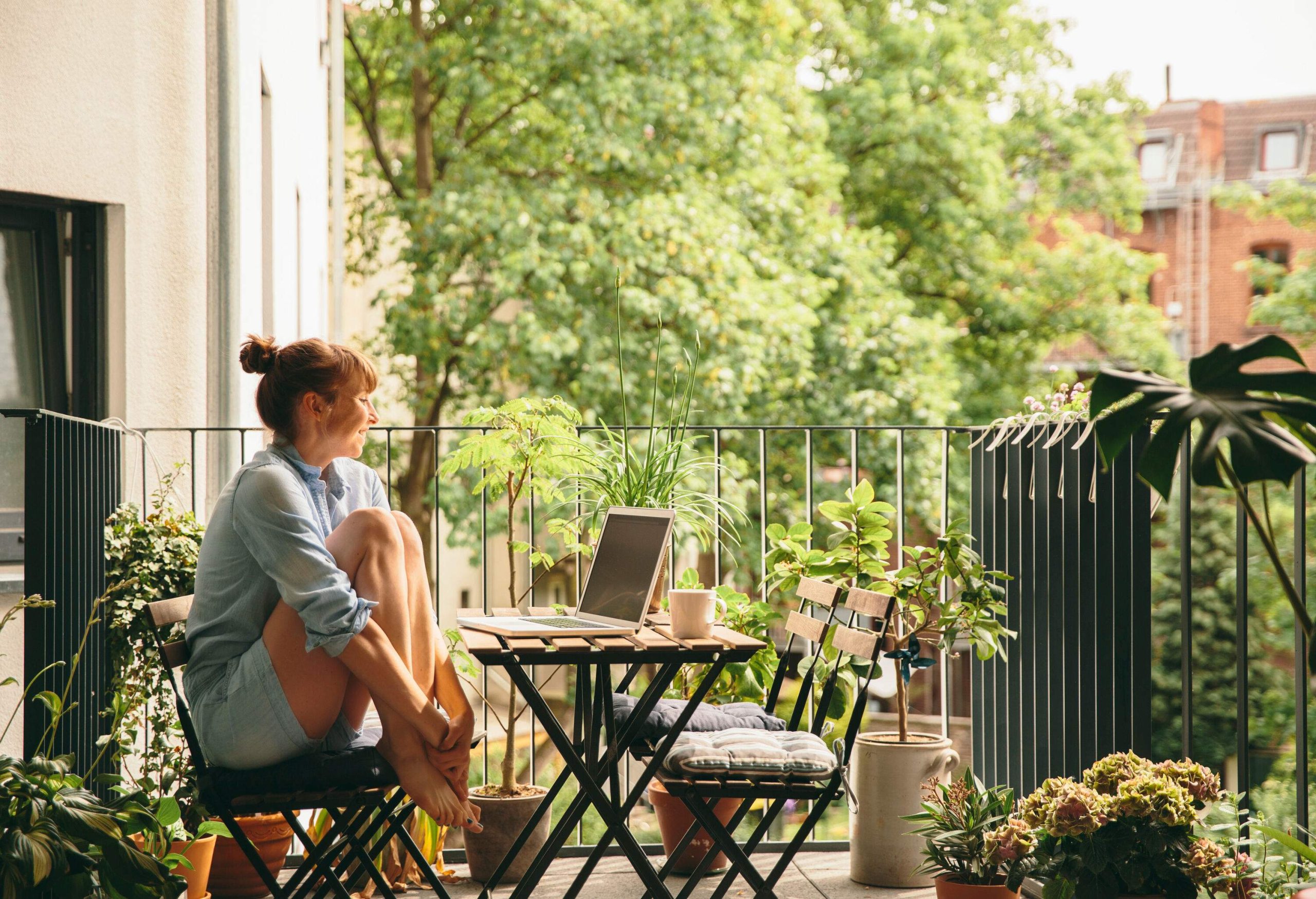 A woman sitting in a garden chair with her feet up, smiling as she watches something on her laptop.