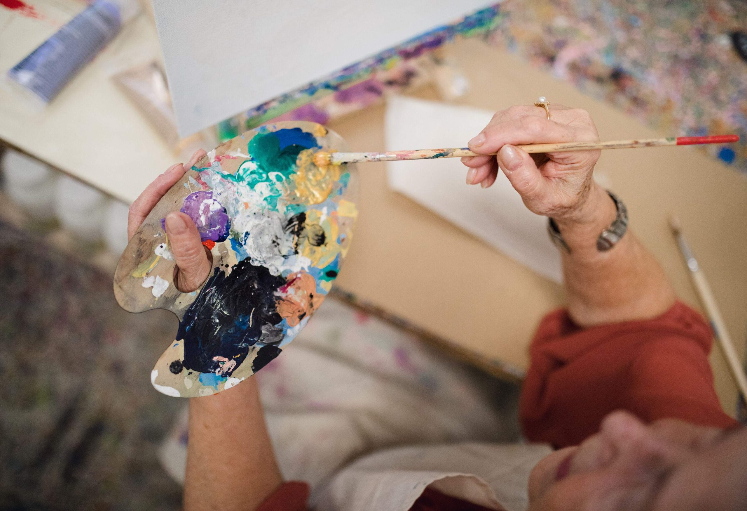 An artist using a brush to mix paint on a wooden mixing board.