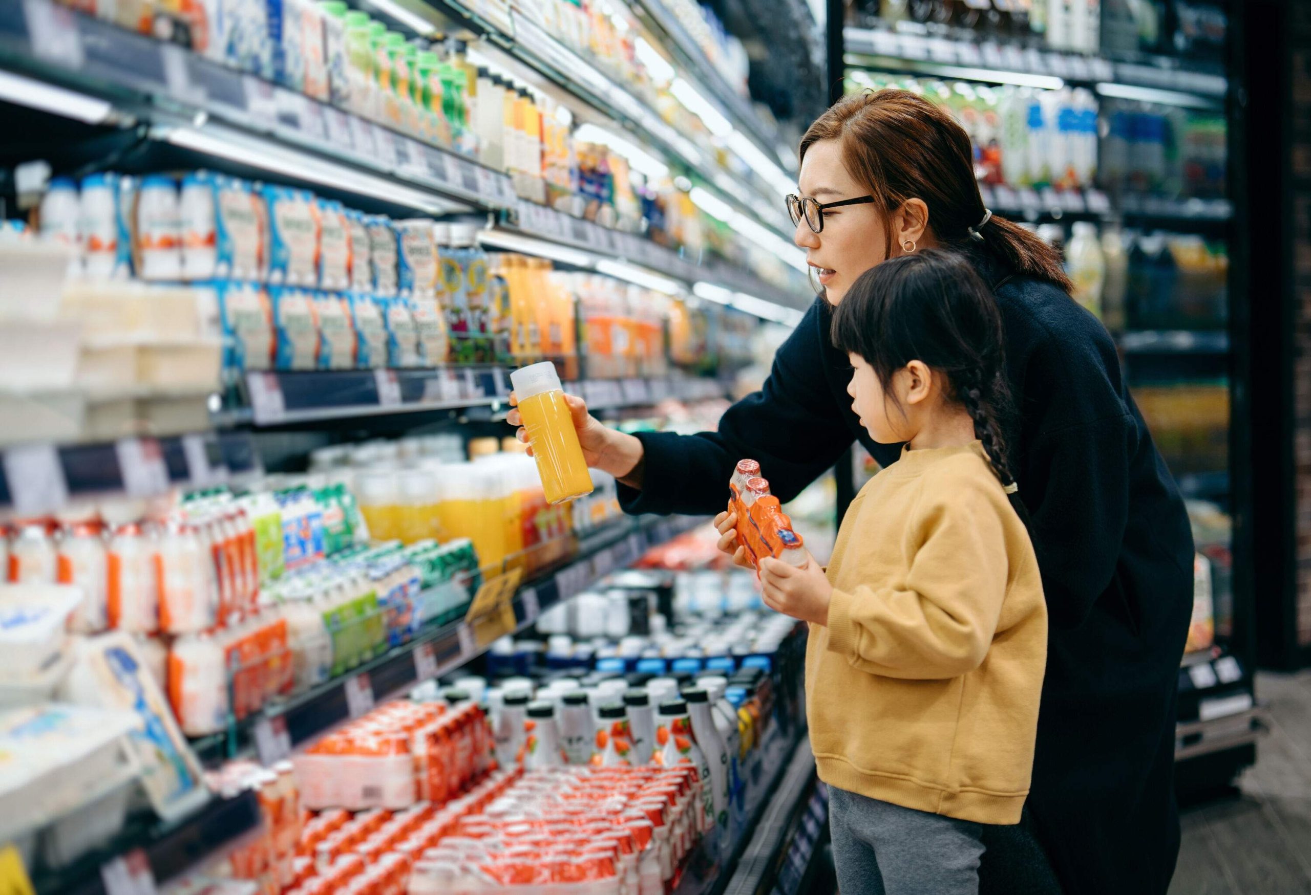 Young mother and her little daughter grocery shopping in supermarket. they are choosing fresh fruit juice together along the beverage aisle. Routine grocery shopping. Healthy eating lifestyle