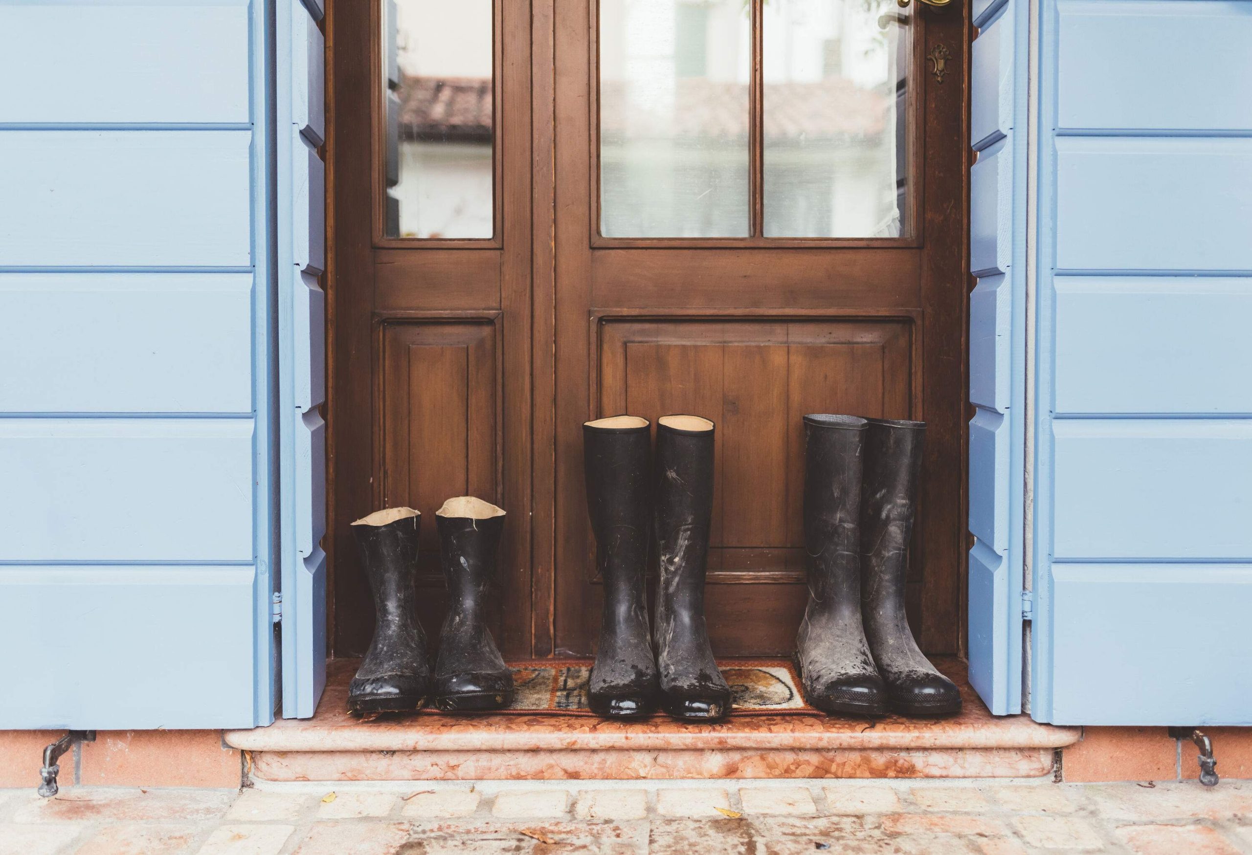 Three pairs of black rubber boots are in front of a wooden door.
