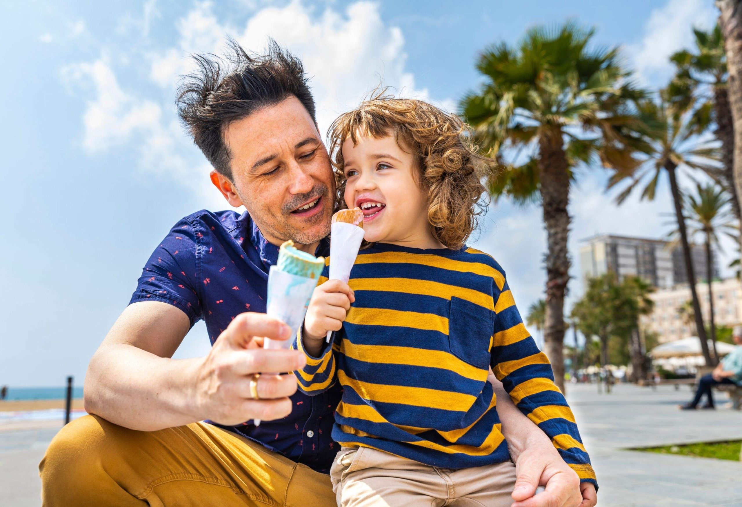 A man and a boy enjoying ice cream on a beach with palmtrees in the background