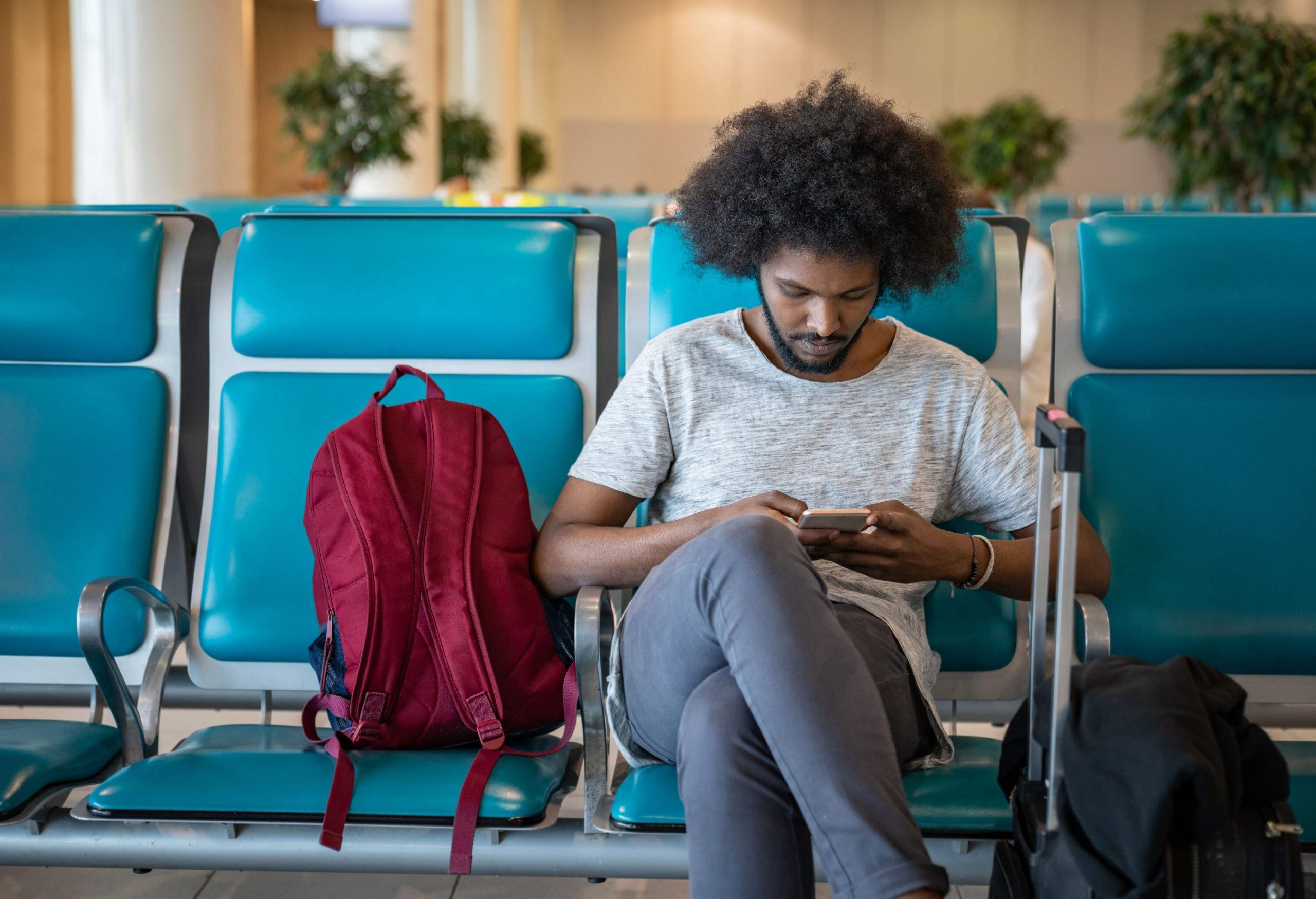 A man focused on his smartphone while sitting next to his bag at a terminal.