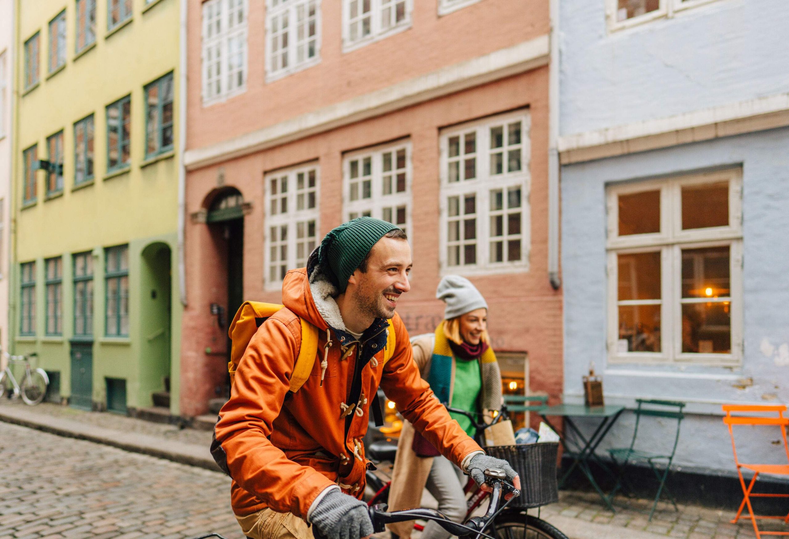 Tourists joyfully ride bicycles along a charming brick street with a picturesque backdrop of colourful buildings.