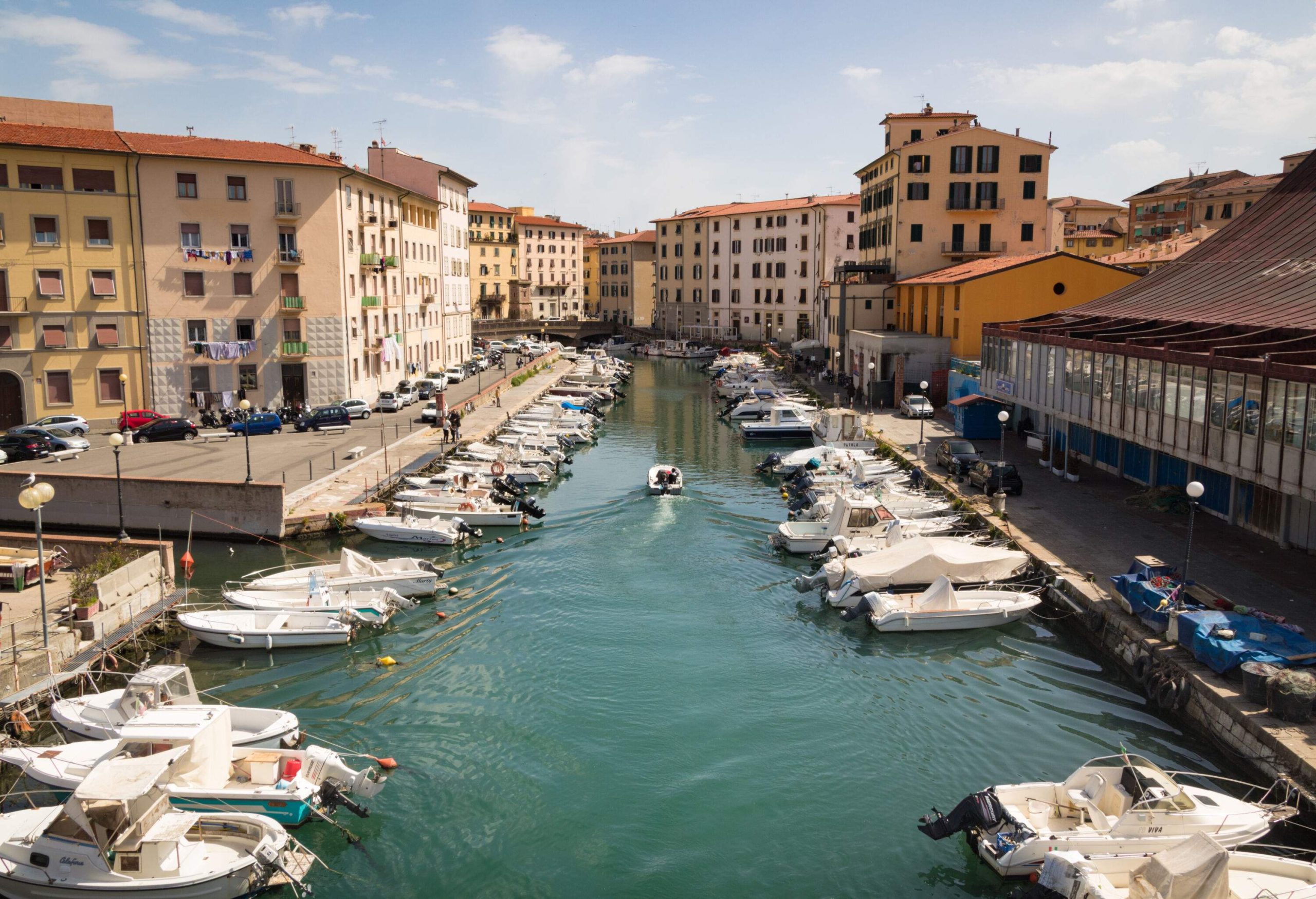 White small boats lined both sides of the canal in the middle of colourful buildings.