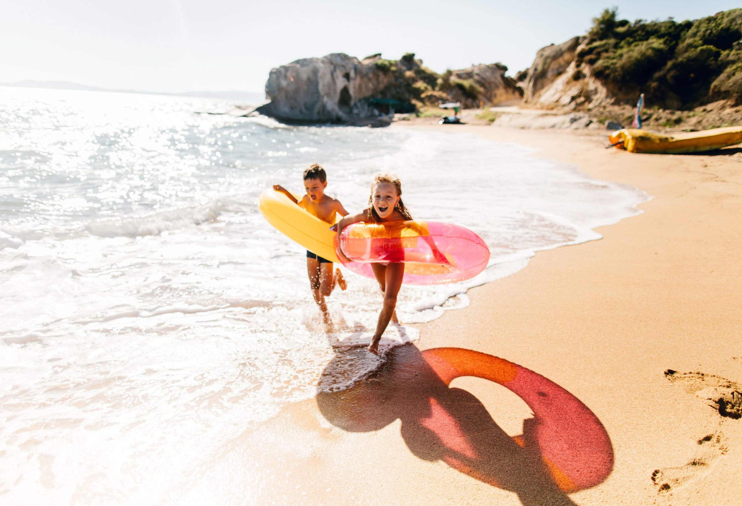 Two joyful kids running on the beach while wearing swimming rings.