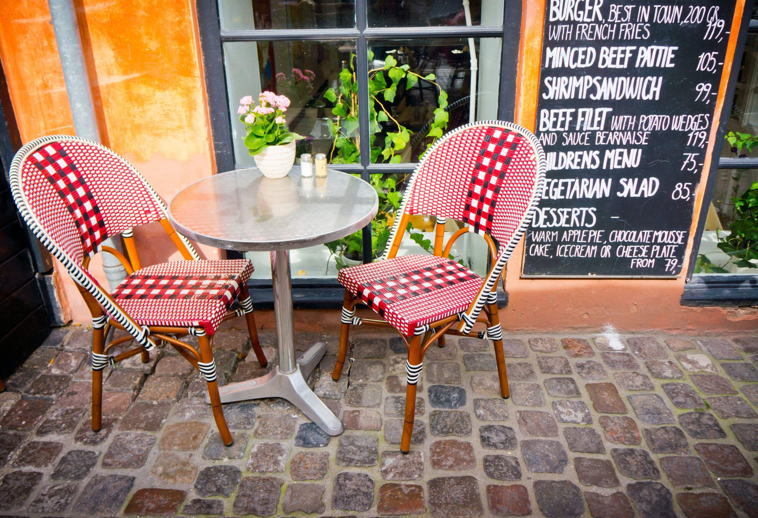 Wooden café chairs and tables next to a menu mounted on the wall.