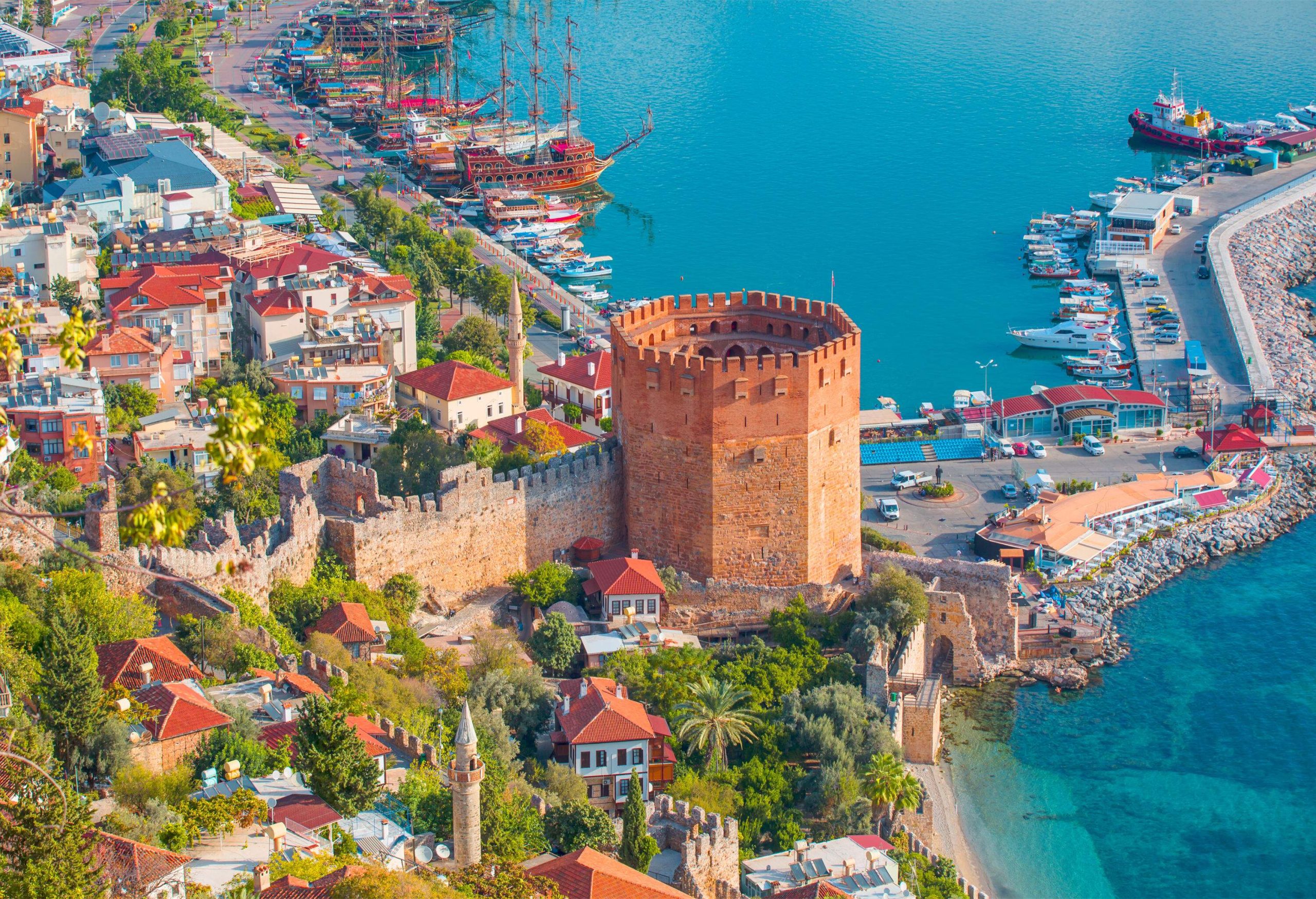 A red brick octagonal tower between a cluster of coastal homes and a harbour full of anchored boats.