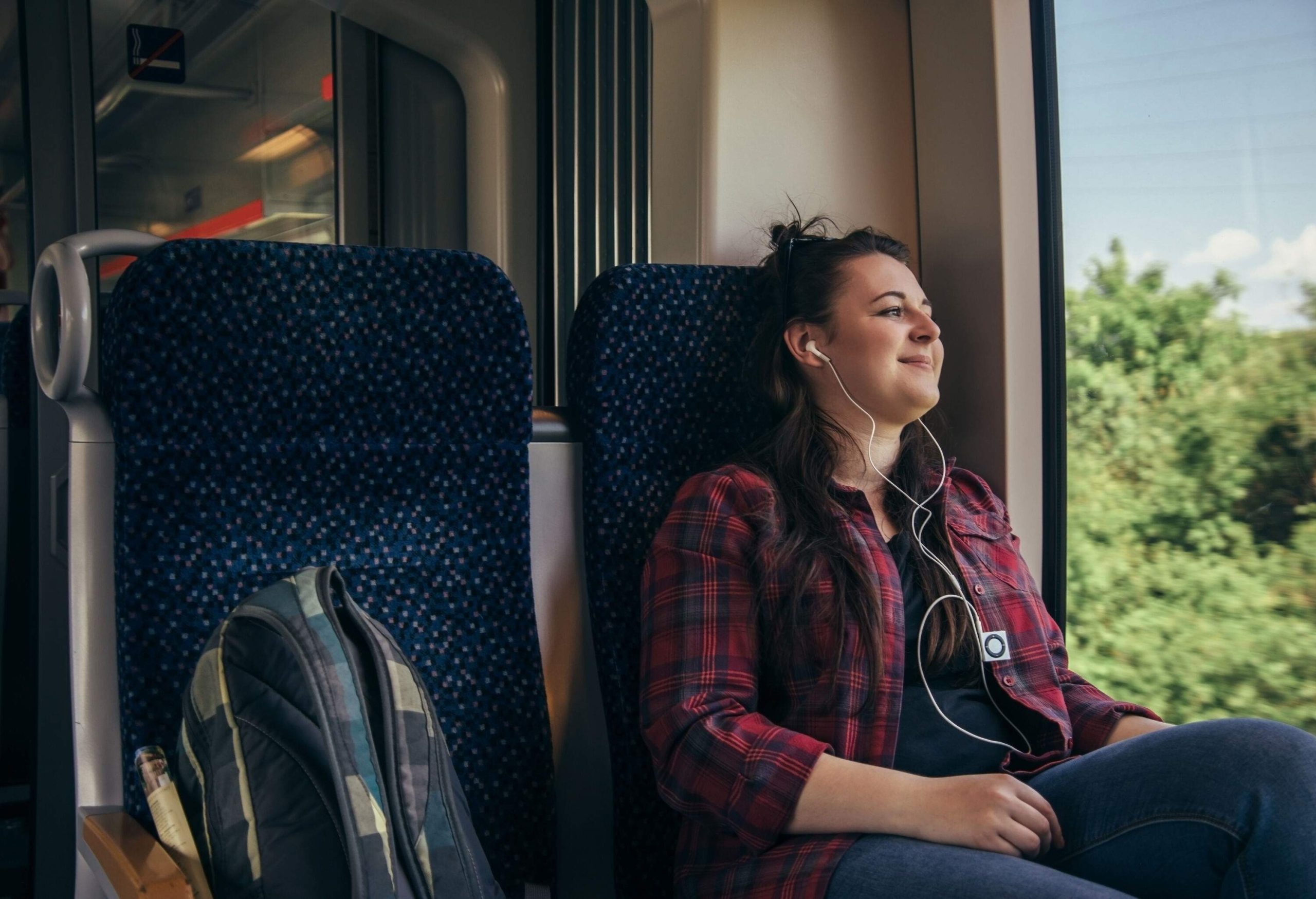 A smiling woman seated on the train gazed out of the window with an earpiece on her ears.