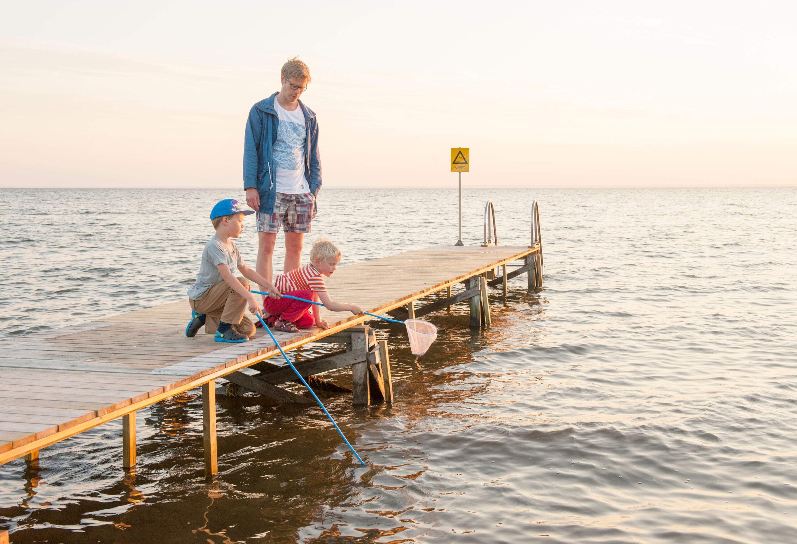 A man standing on a pier and watching two young kids use landing nets to catch a fish.