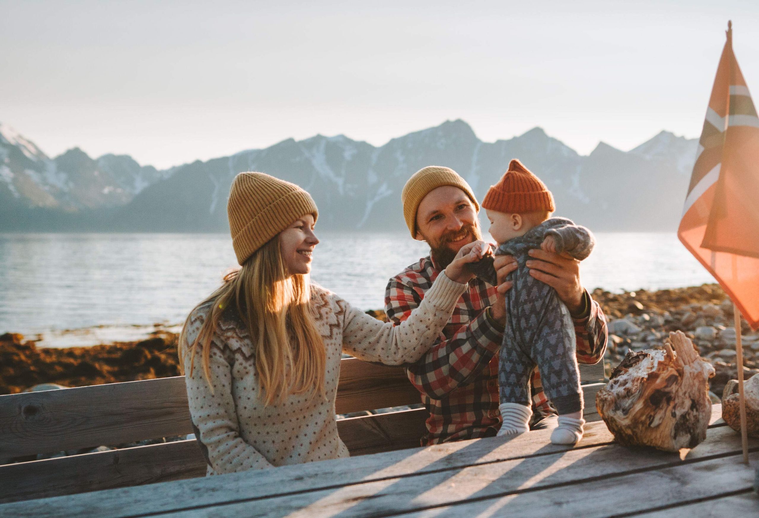 A family of three in warm clothes sits on a chair, with the man holding the baby on the table.