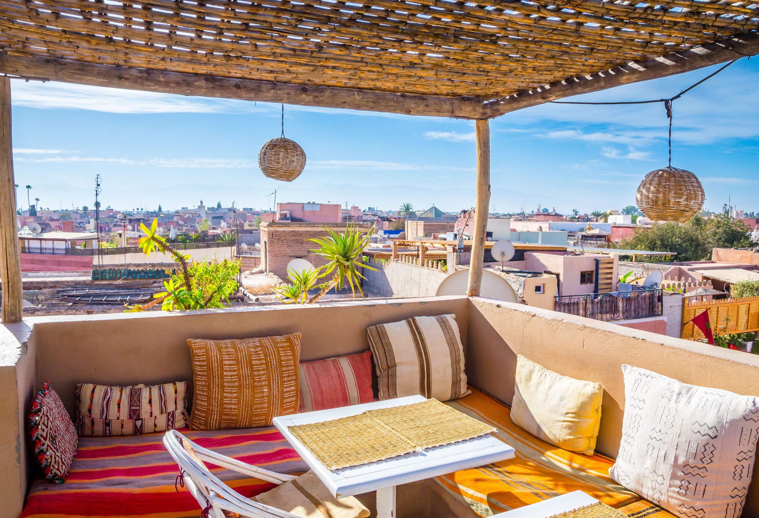 A traditional rooftop cafe has tables and chairs with colourful cushions and views of the city skyline.