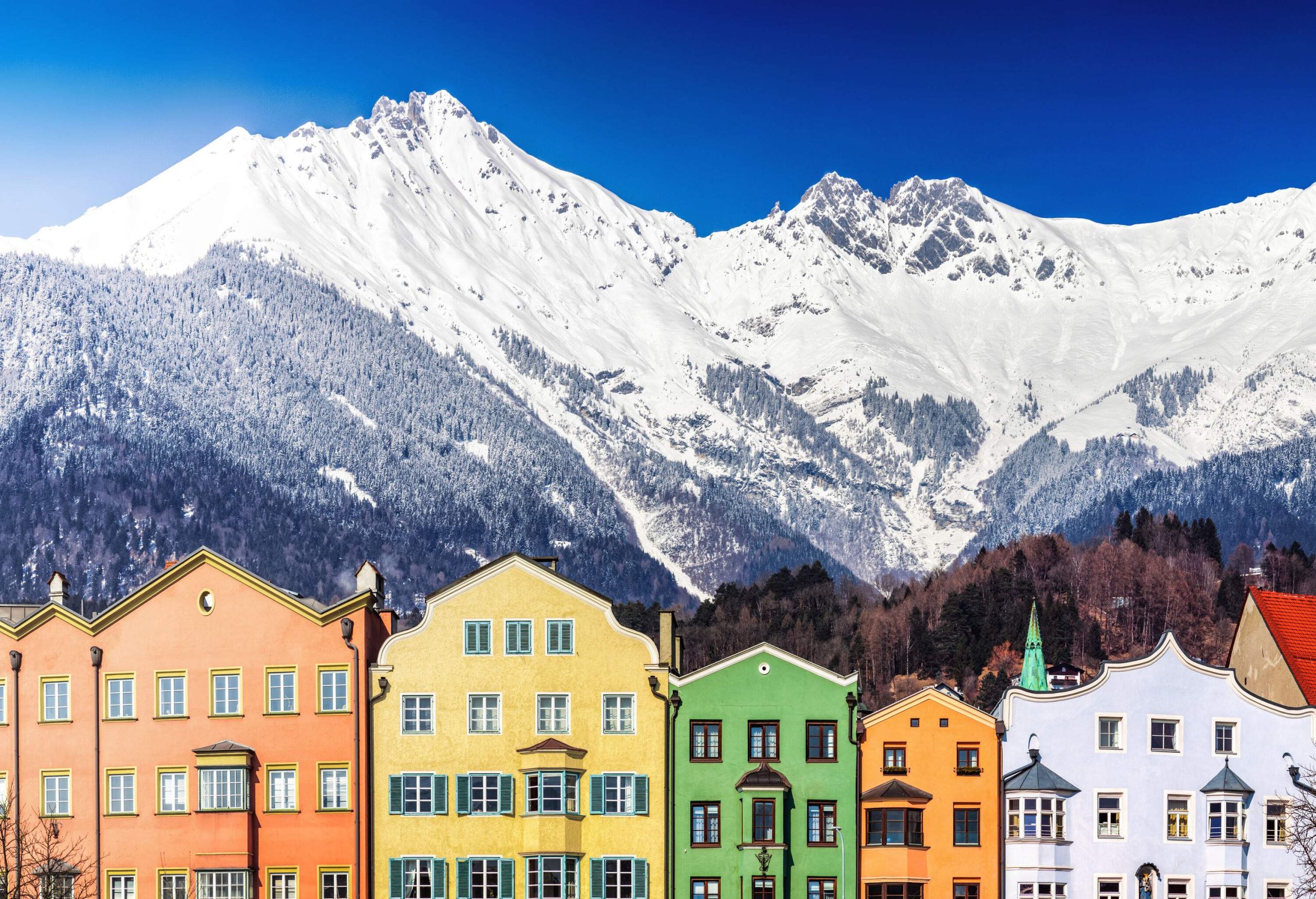 A snow-covered mountain range behind a row of houses with colourful façades.
