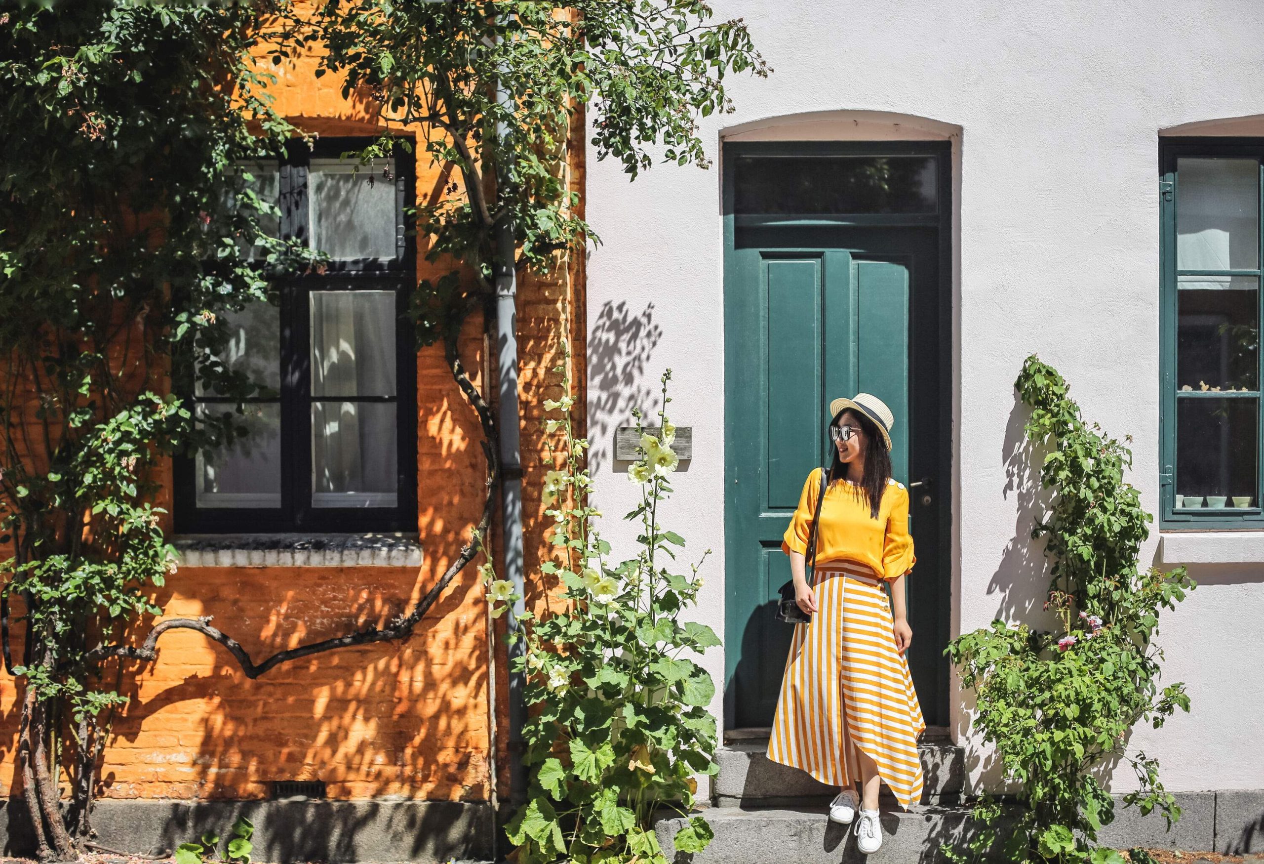 A smiling young lady steps down in front of a green door on a sunny day.