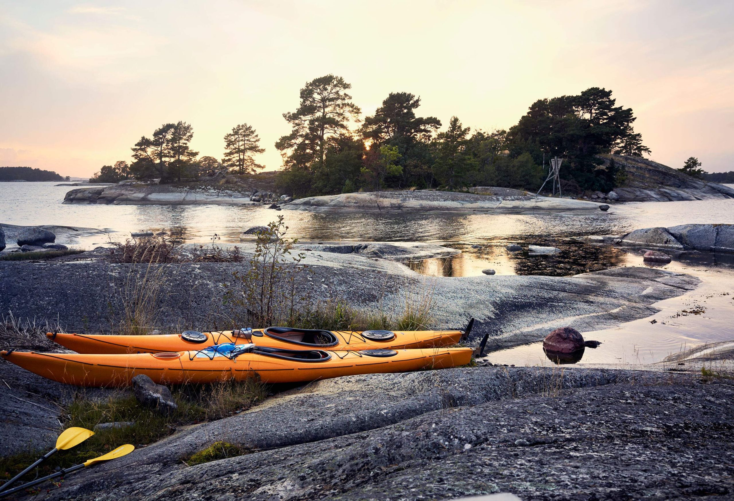 Two yellow kayaks parked on a flat rock beside a calm river.