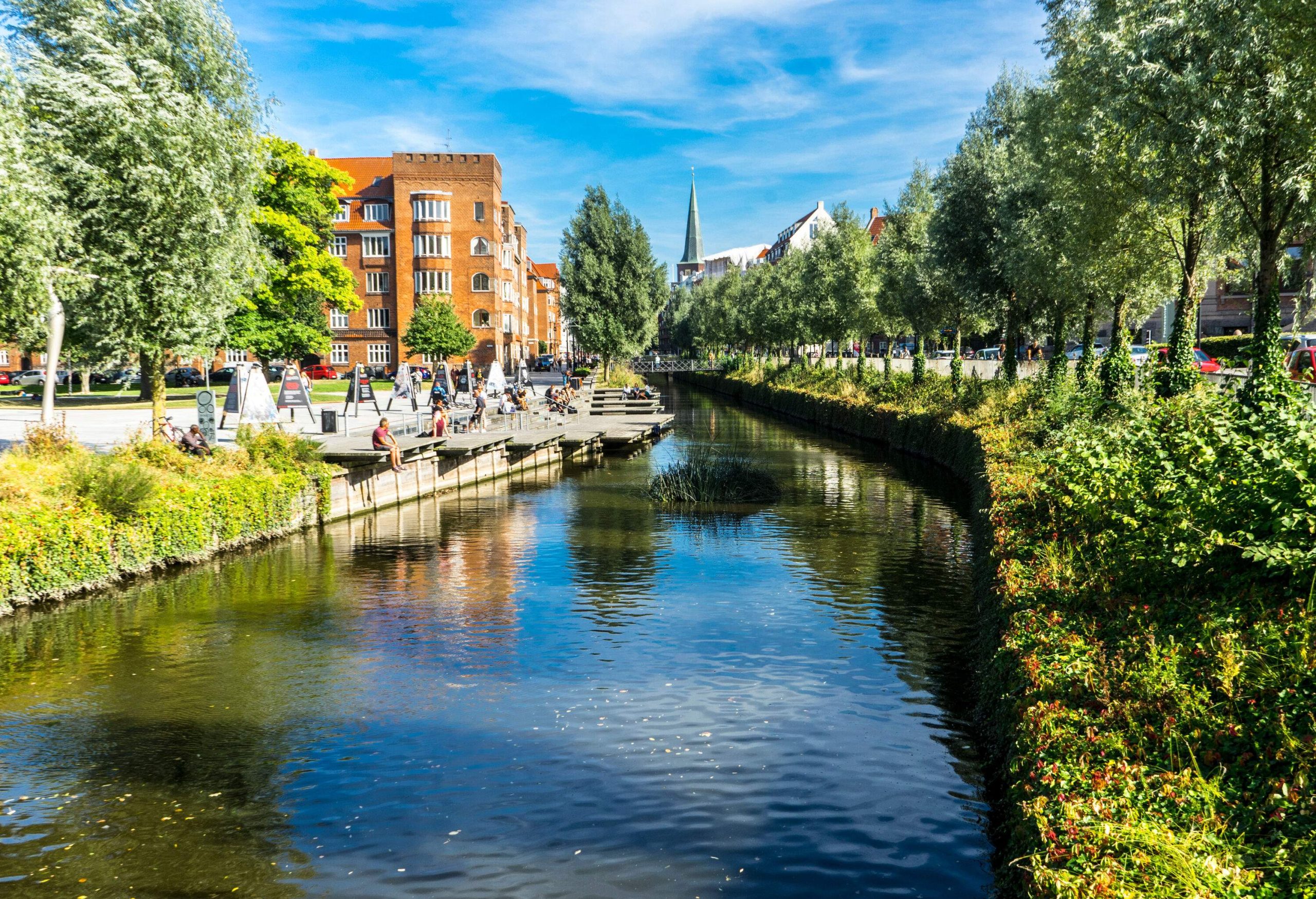 A river canal along a promenade surrounded by buildings and trees.