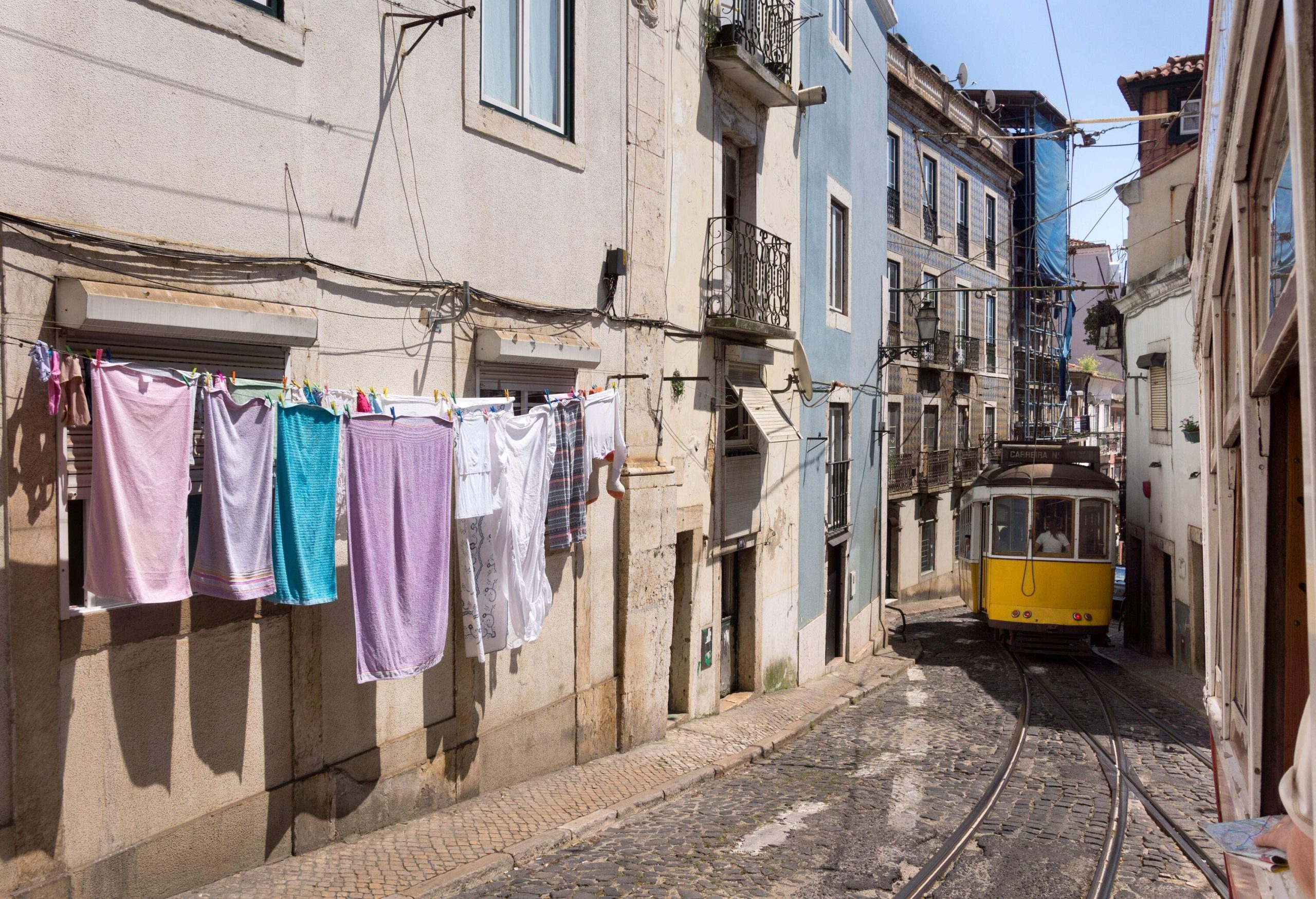 A classic tram passes through a narrow street lined with traditional houses with hanging clothes outside.
