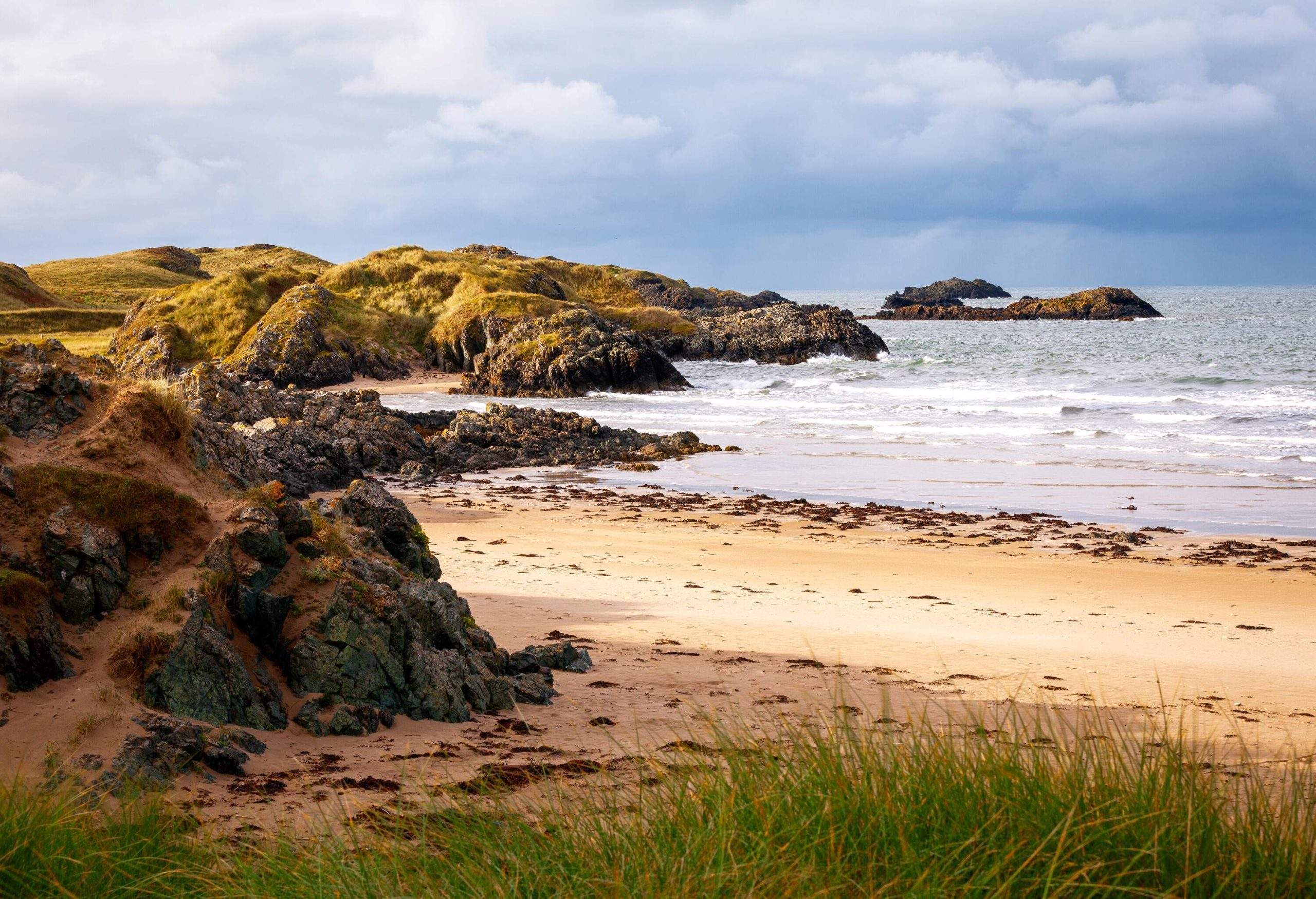 View of rugged coast and beach with boulders covered in moss on a cloudy windy day