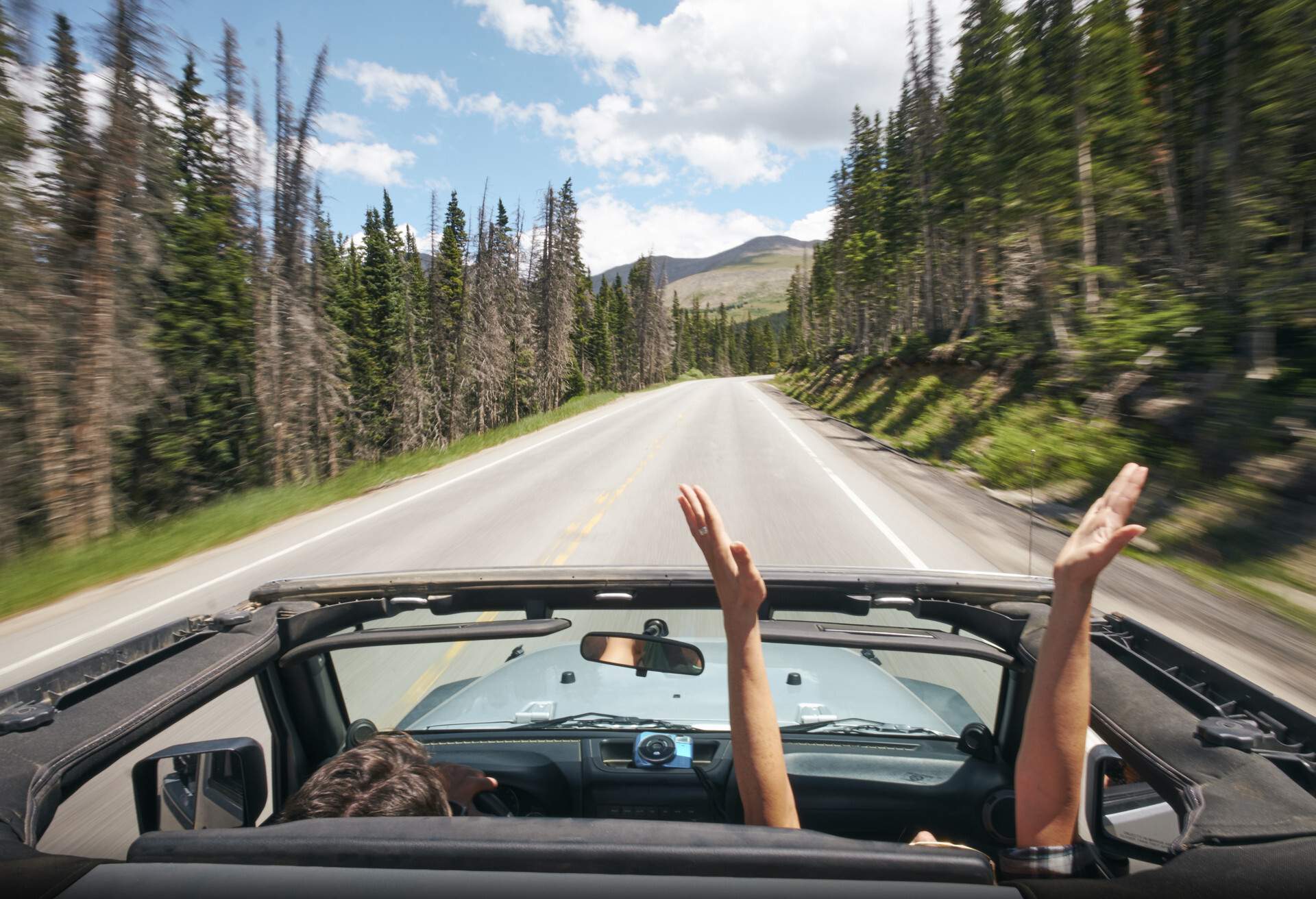 A man in the passenger seat stretching his arms over his head as they drive down the road.