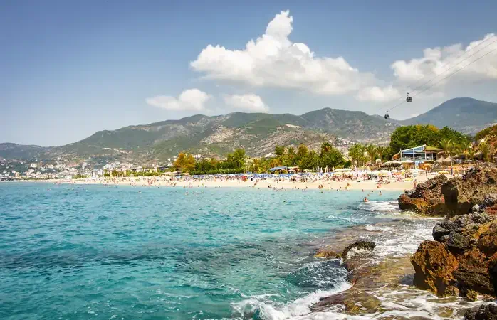 Landscape of resort sea beach in lagoon bay on summer sunny day. Rocky beach and mountains on horizon in tropical sea town. Beautiful paradise nature of Turkey perfect for relax