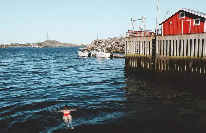 Woman swimming in cold ocean near fishing village on Lofoten Islands