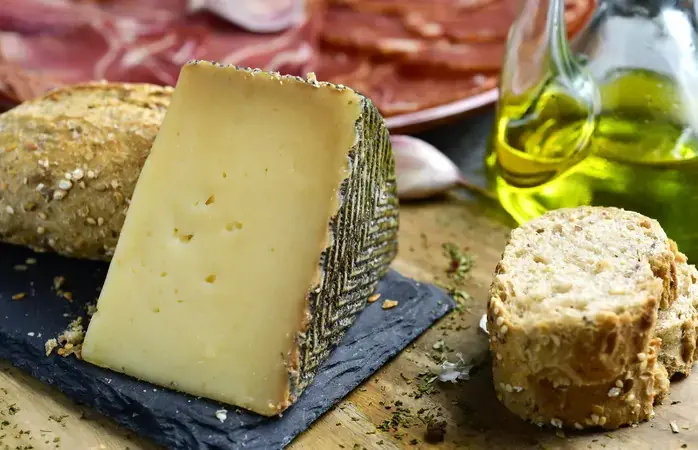 closeup of a piece of manchego cheese, some slices of bread, a cruet with olive oil and a plate with an assortment of different spanish cold meats as chorizo, cured pork tenderloin and serrano ham; Shutterstock ID 570077260