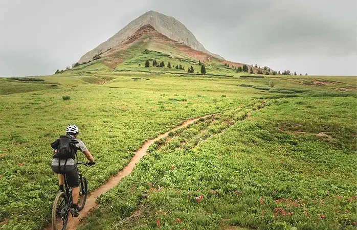 a man rides his mountain bike through a beautiful green meadow beneath rocky mountain peak. horizontal mobilestock composition taken in the san juan range of the colorado rocky mountains. durango, colorado.