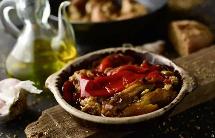 a plate with escalivada, a typical dish of Catalonia, Spain, made with grilled and peeled eggplant, red pepper and onion, on a rustic wooden table next to a cruet with olive oil