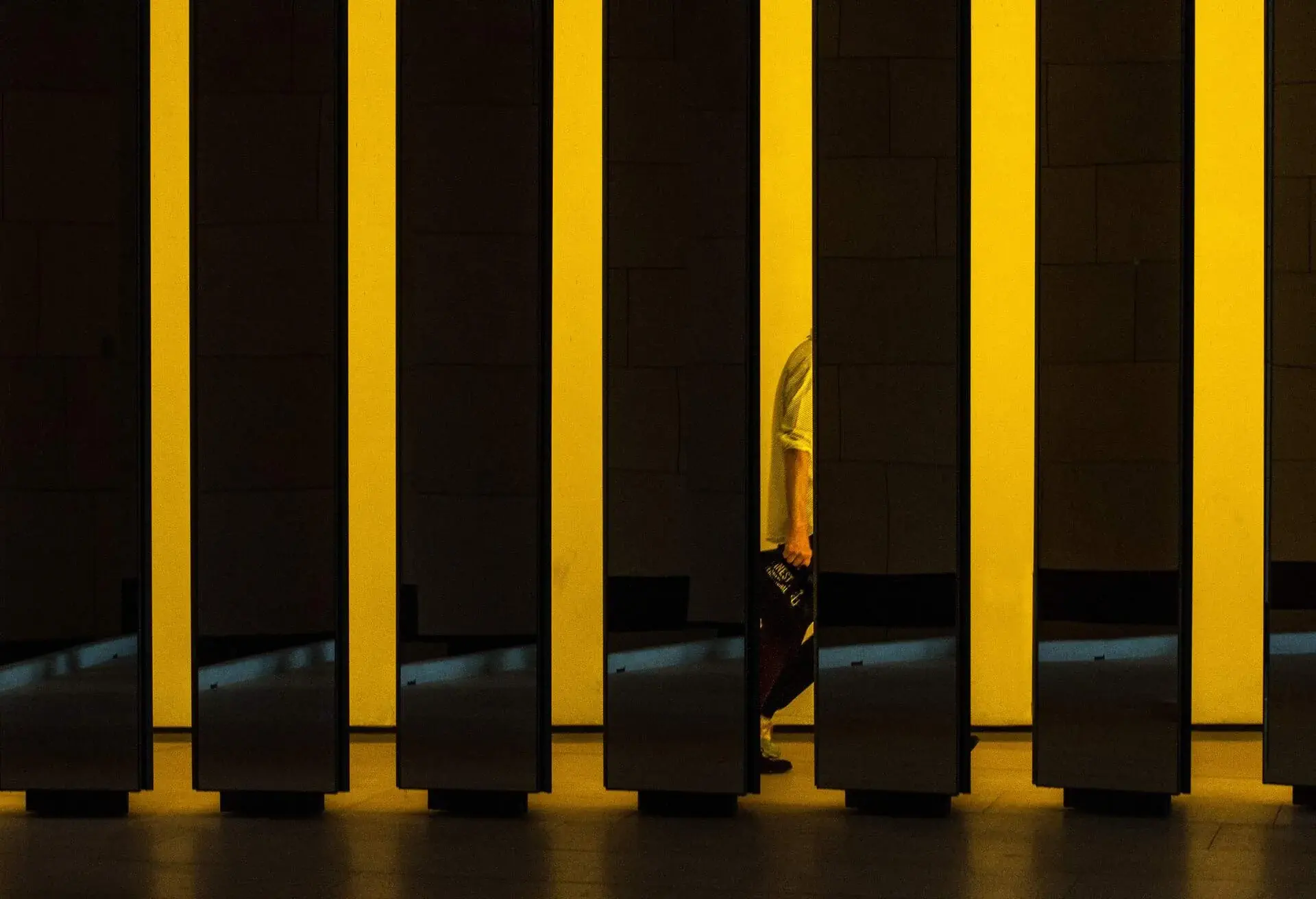A series of yellow columns, one of which has a reflection of a person's half-body.