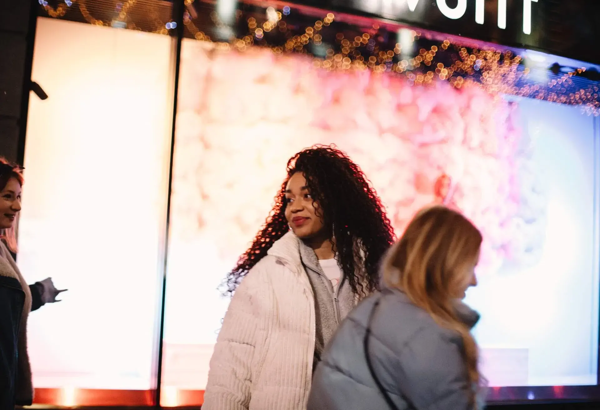 Person with curly hair and a white jacket smiled and looked back at her friends.