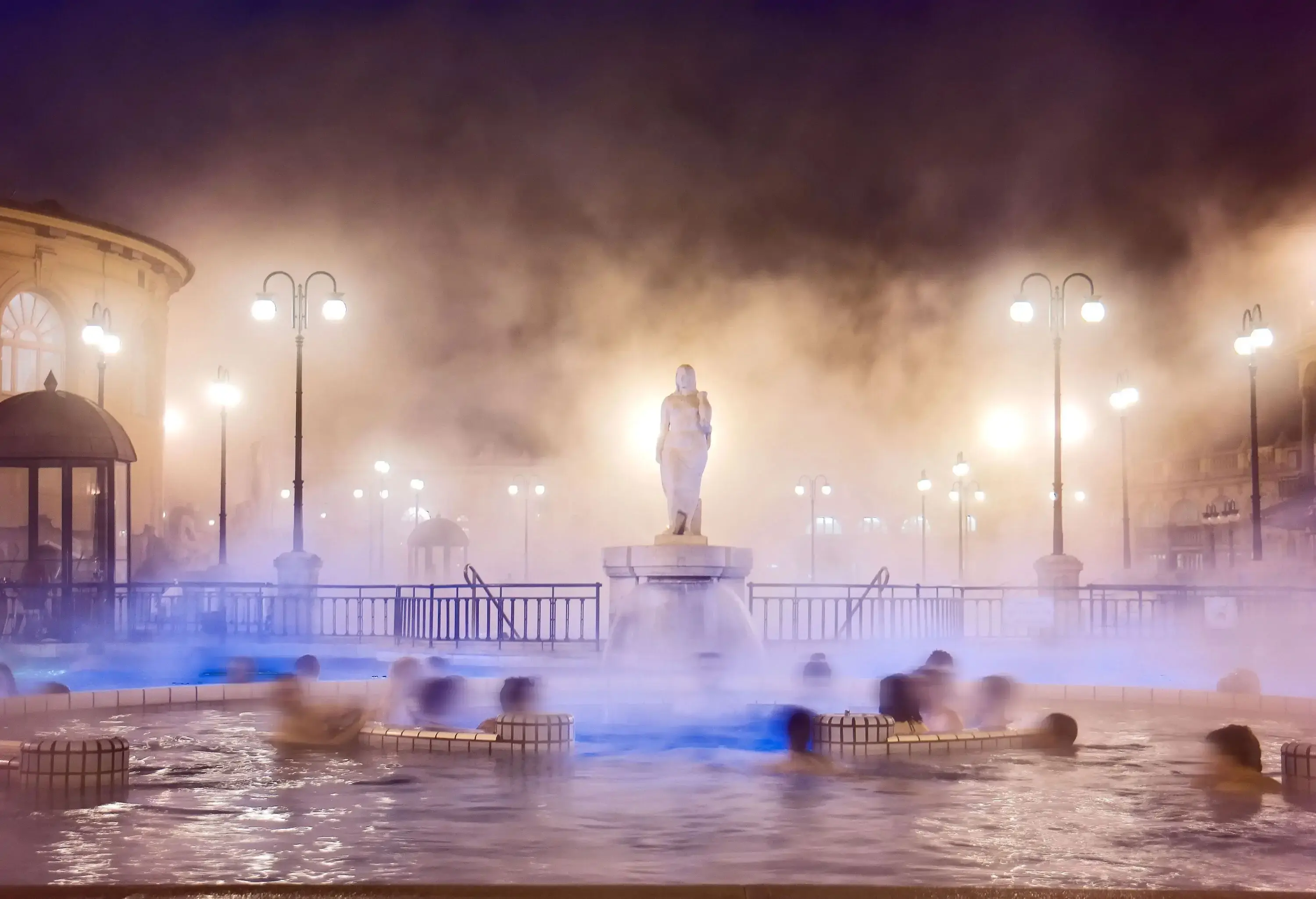 People submerged in the swimming pool of a foggy thermal bath complex.