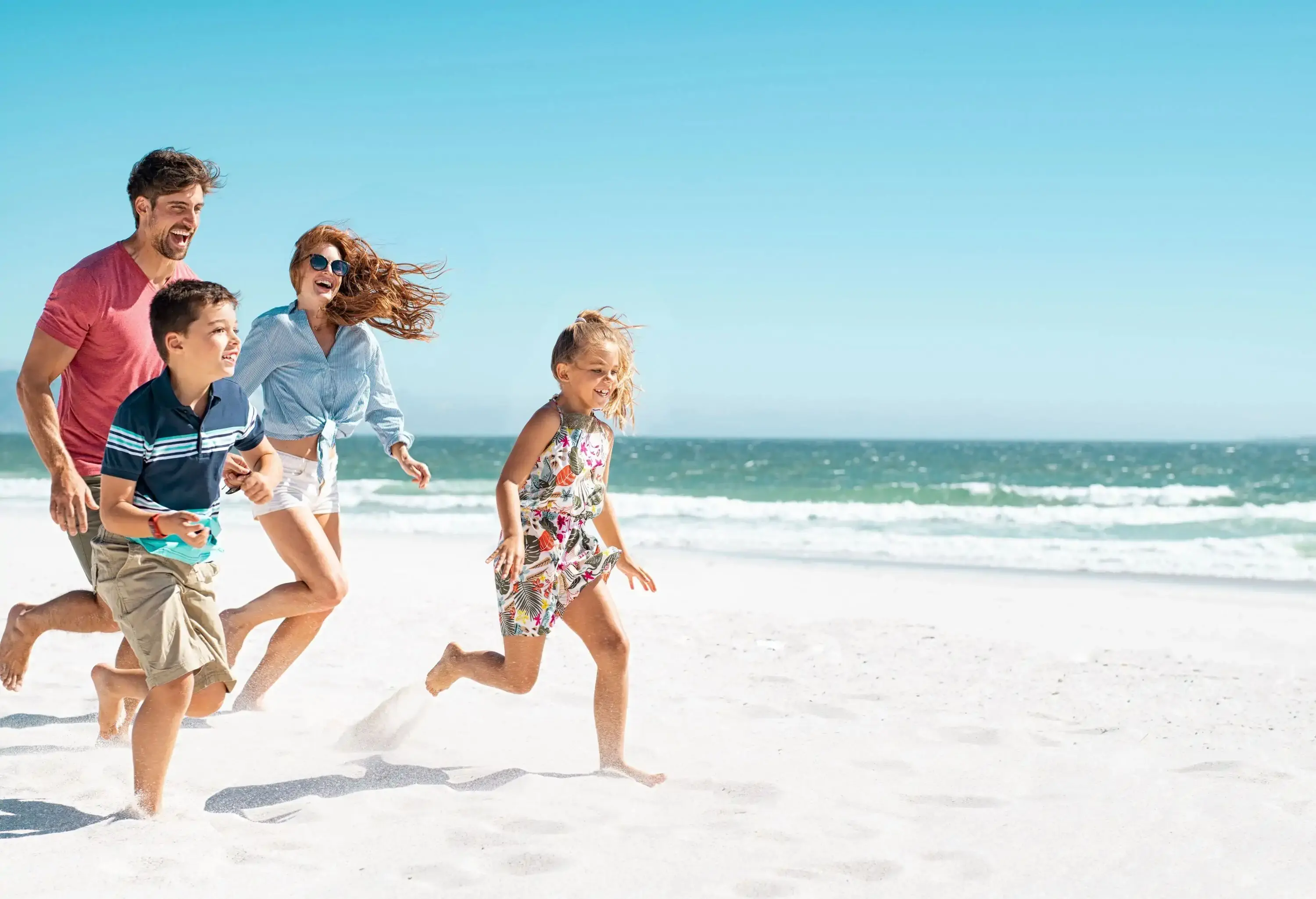 A family of four running on the white sandy beach.