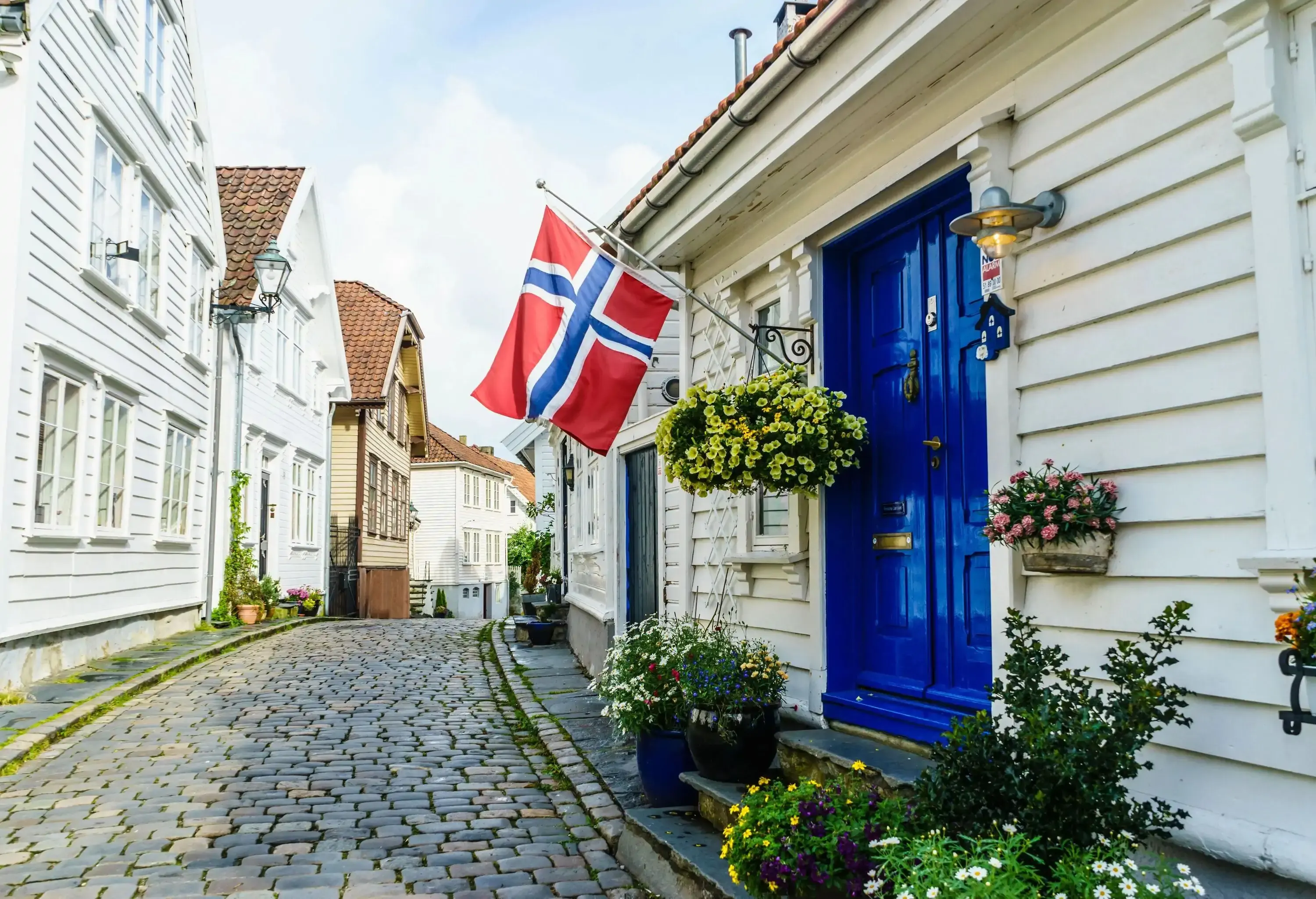 A narrow cobblestone alley with a blue door and a norwegian flag