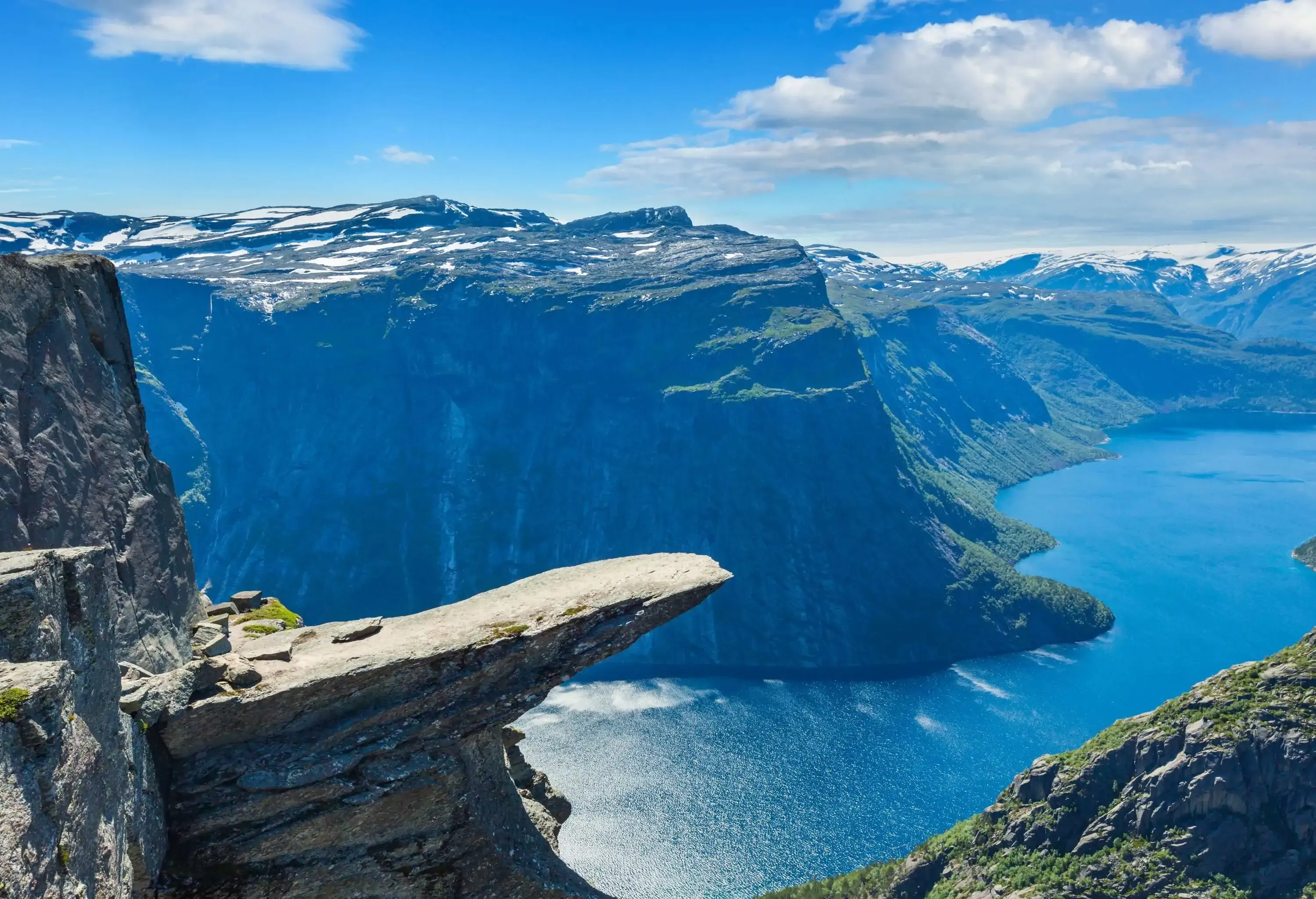 A flat-topped rock formation protrudes from a cliffside with views of a lake below.
