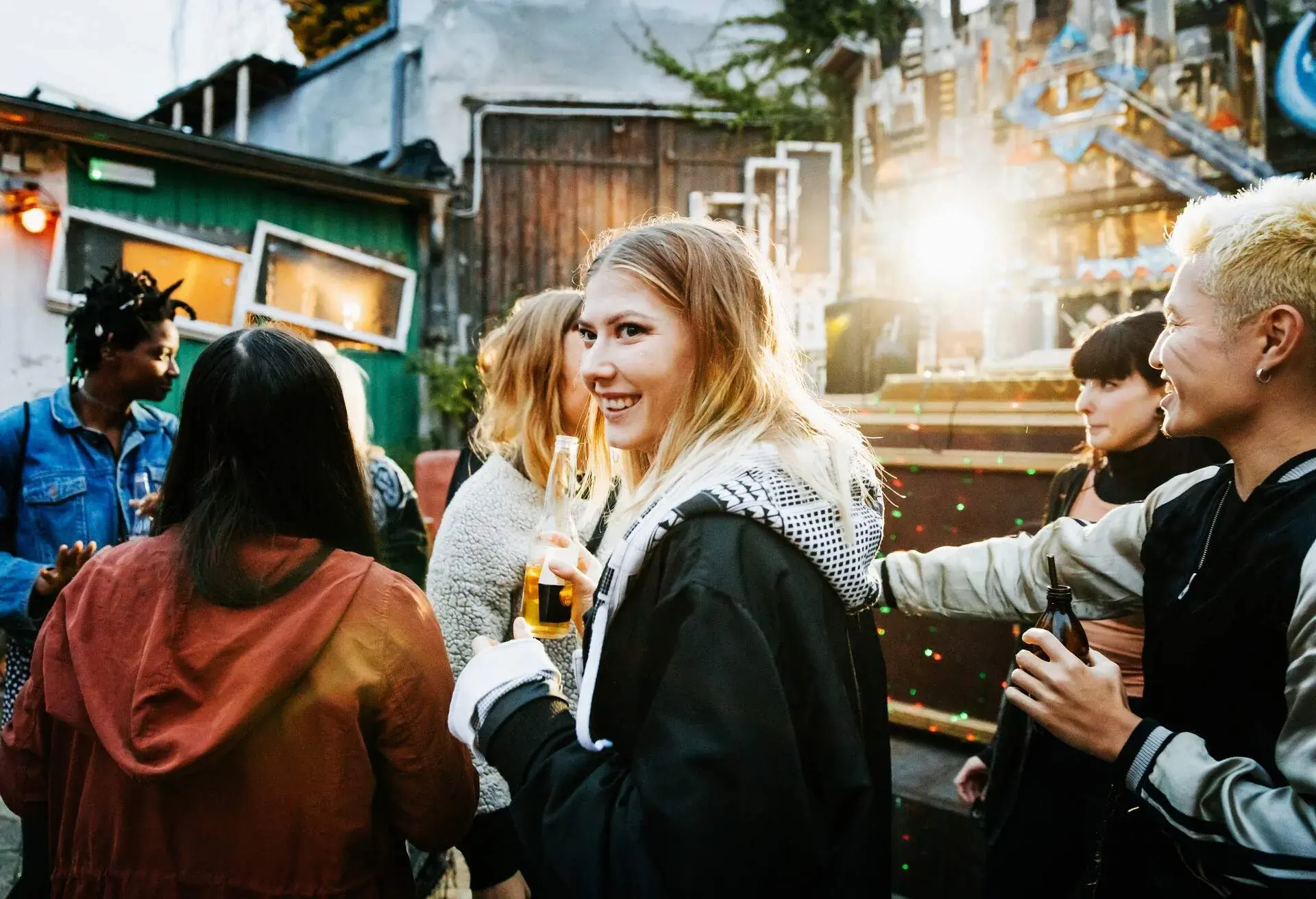 A blonde woman smiles while holding a bottle of beer as she dances with her friends in an open air nightclub.