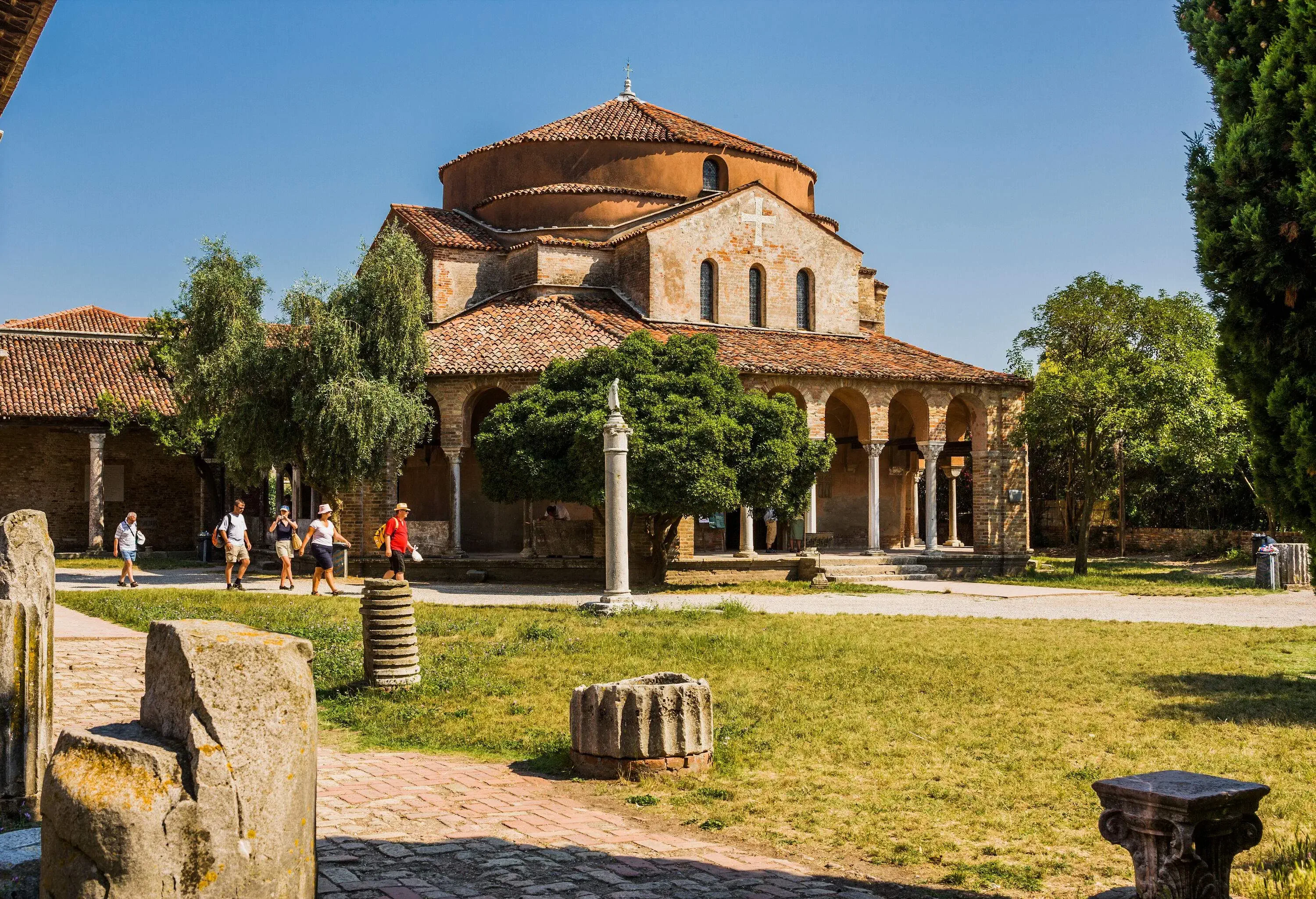A group of people strolling down a path that runs alongside a Byzantine-style church with tiled roofs.
