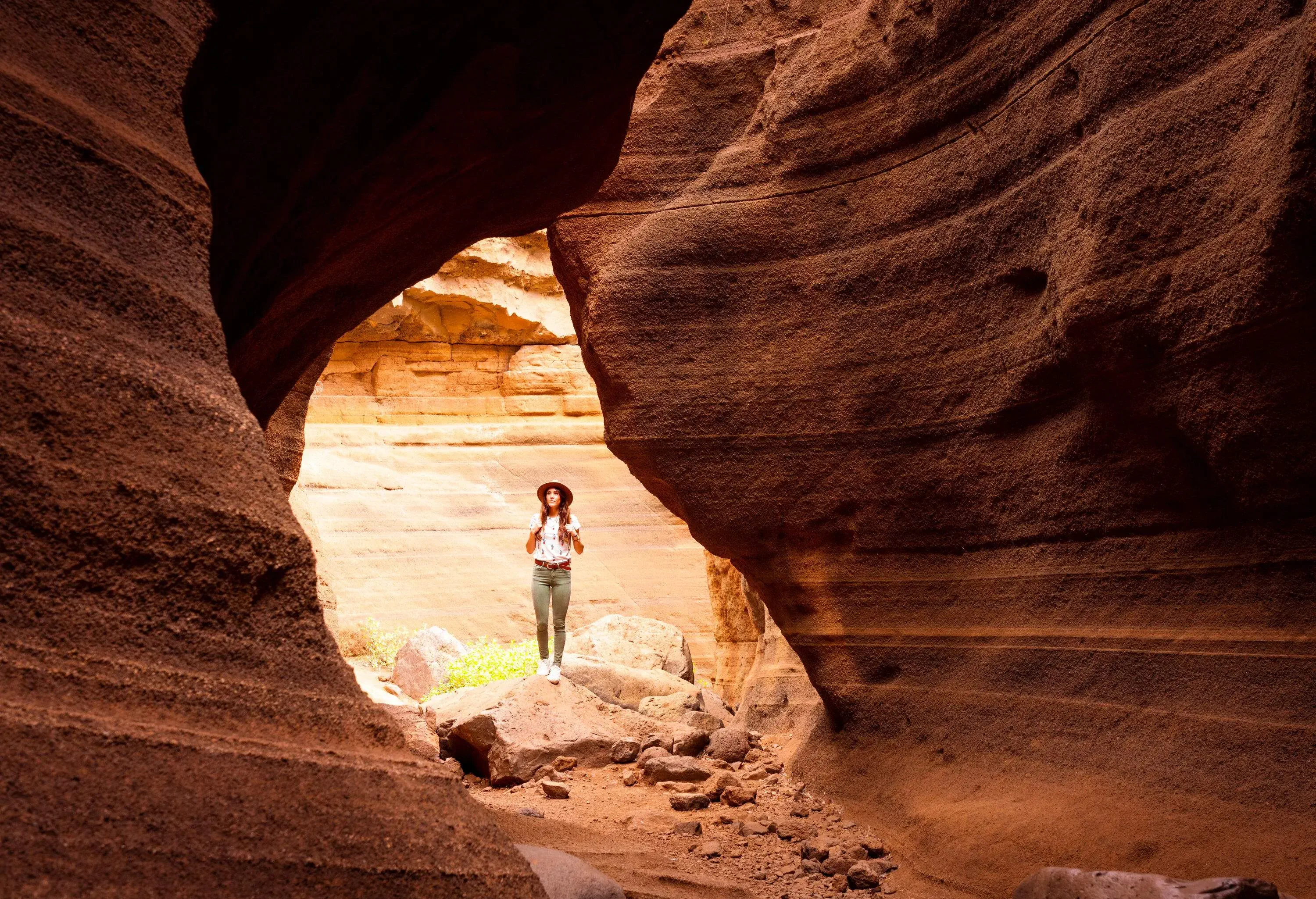 A female hiker wearing a hat standing on a rock in the middle of a canyon.