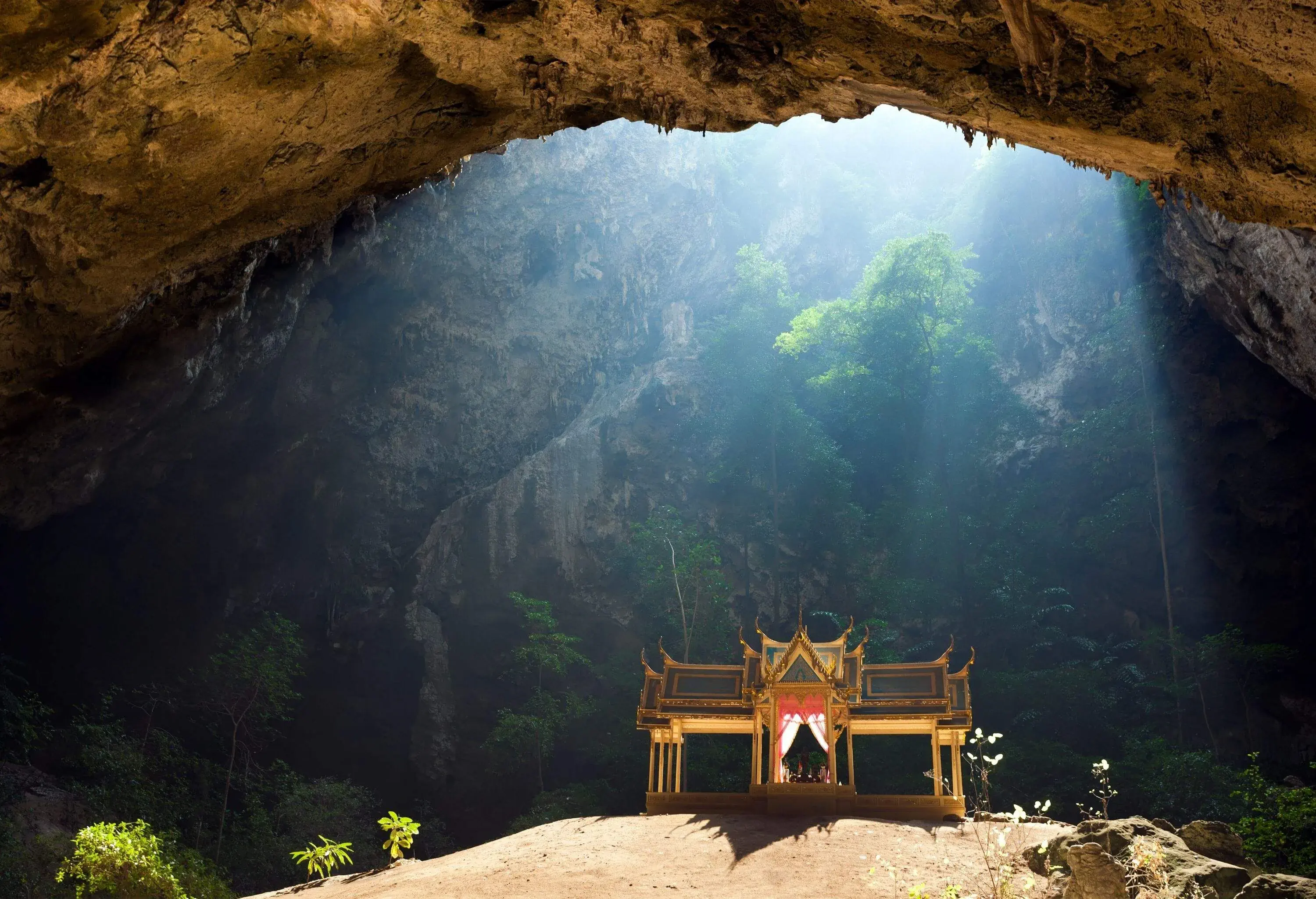 A Buddhist pavilion inside a cave illuminated by sunlight from above.