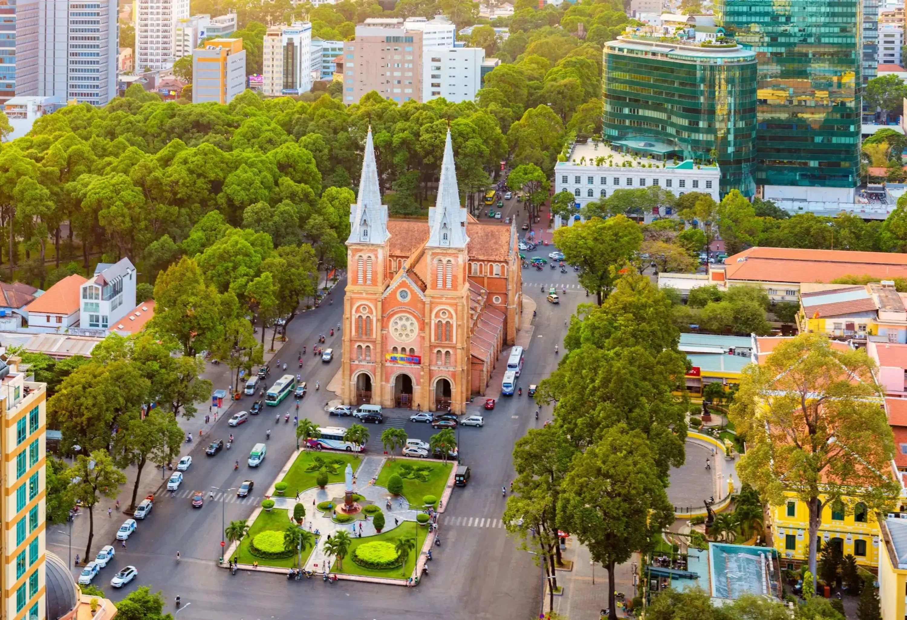 Aerial view of an old city with a mixture of classic and modern structures with a magnificent Catholic cathedral constructed with elegant French bricks, showcasing two impressive Romanesque bell towers, stands as a centrepiece enveloped by lush foliage.