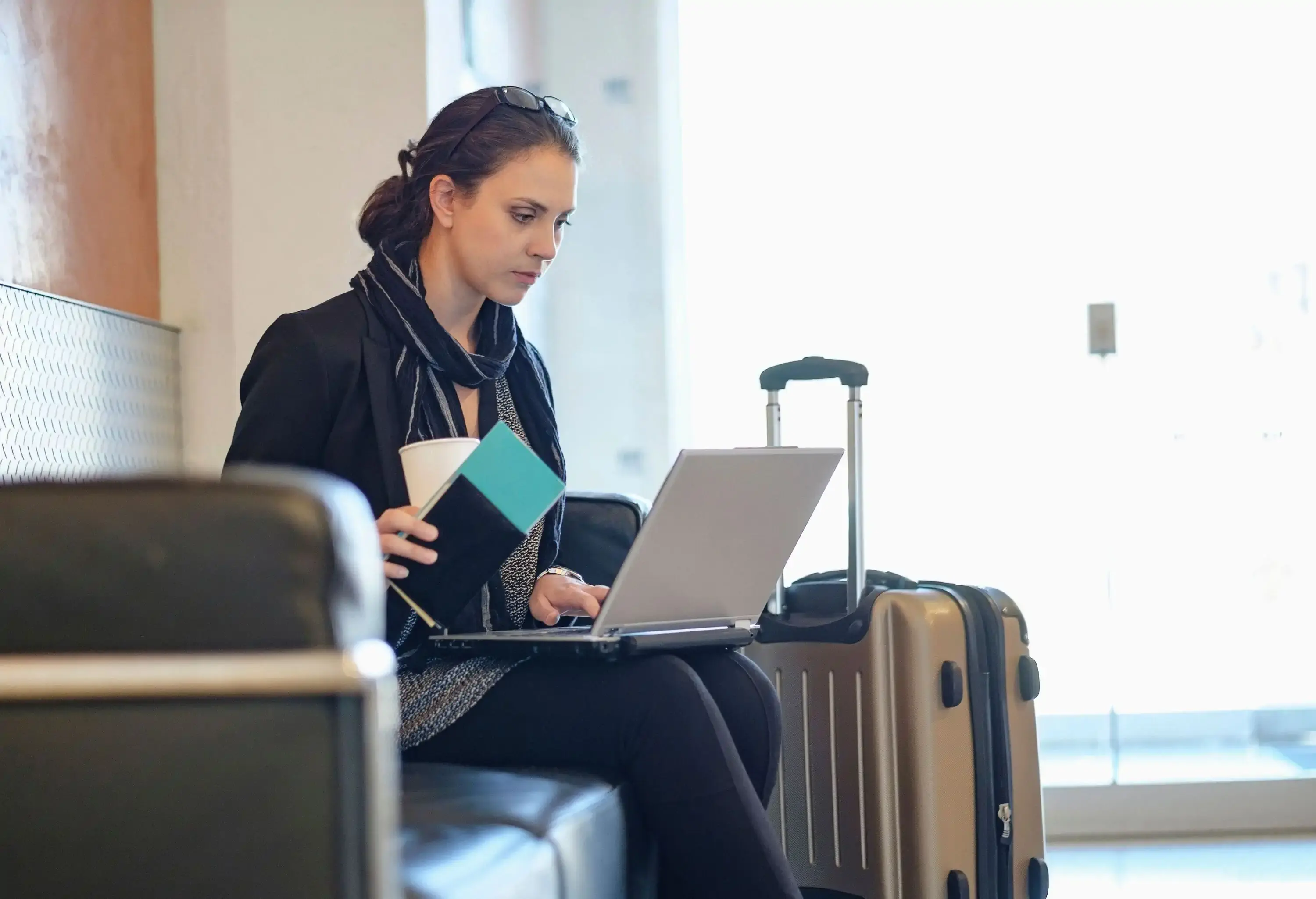 An individual sits on a sofa holding a passport and a laptop.