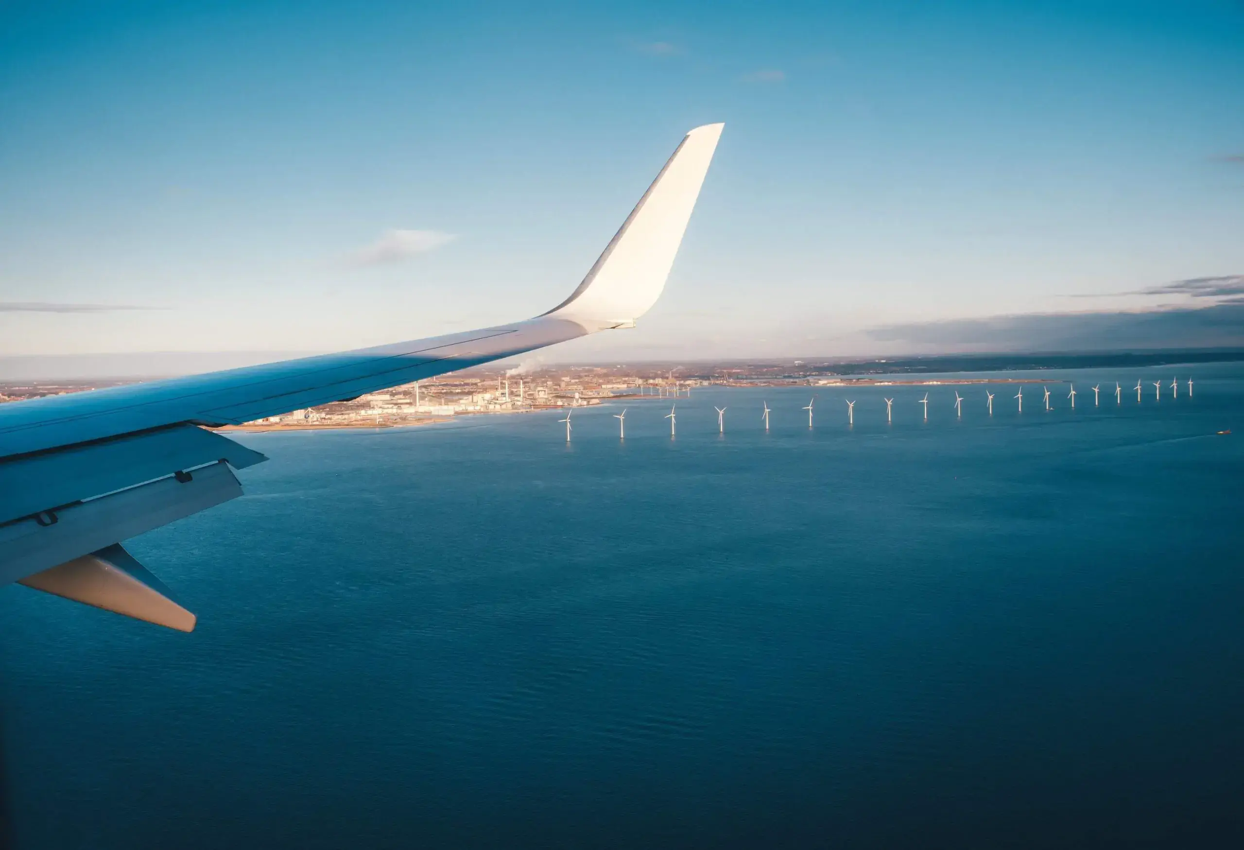 A plane's wing overlooks a sea, including a row of offshore wind turbines.