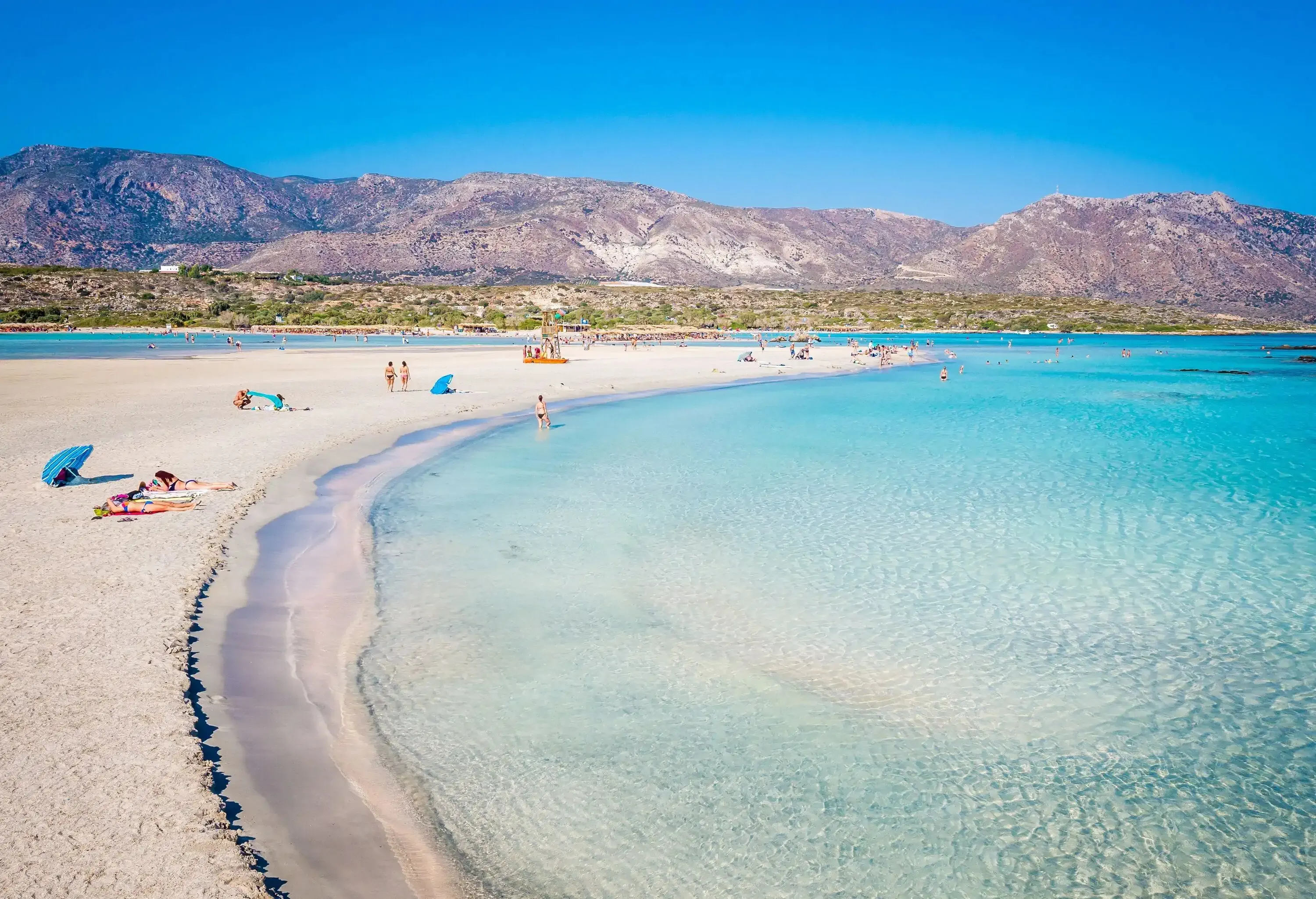 People lounge on a beach with turquoise waters.