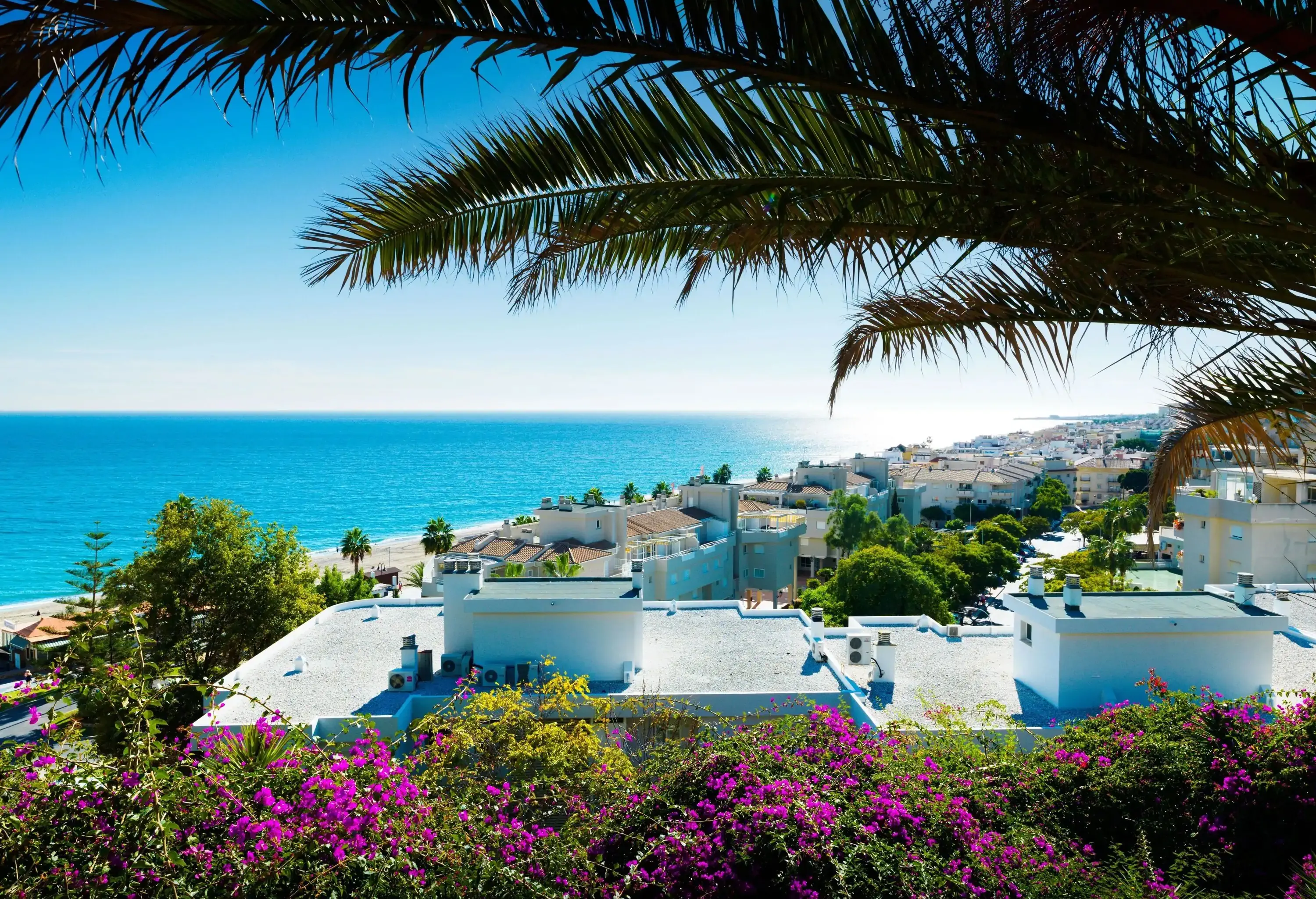 A coastal cityscape with whitewashed houses and the serene blue sea seen from a rooftop.