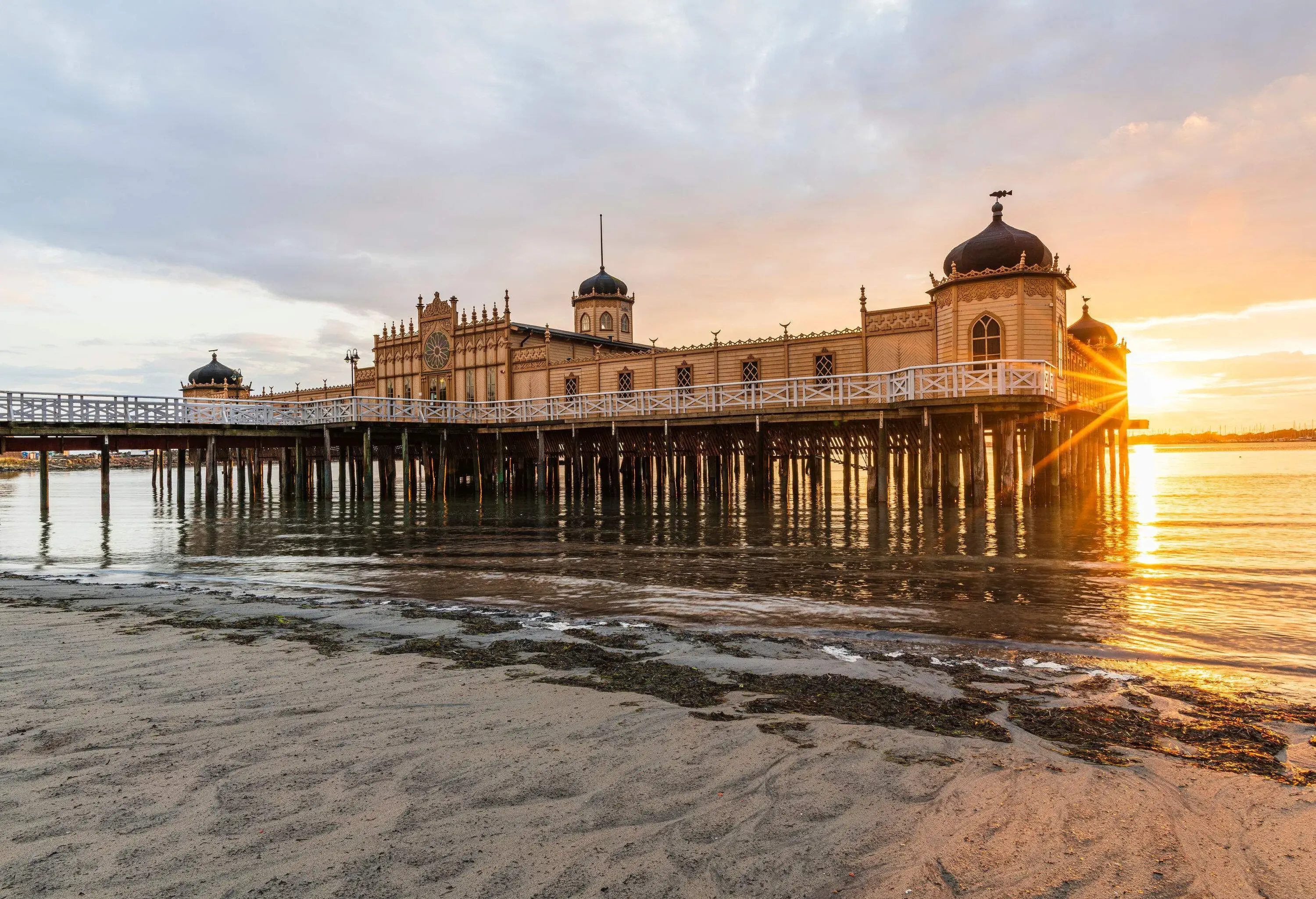 The Moorish-inspired Varbergs Kallbadhus is a bathhouse on stilts located on a beach with the sun shining behind it.