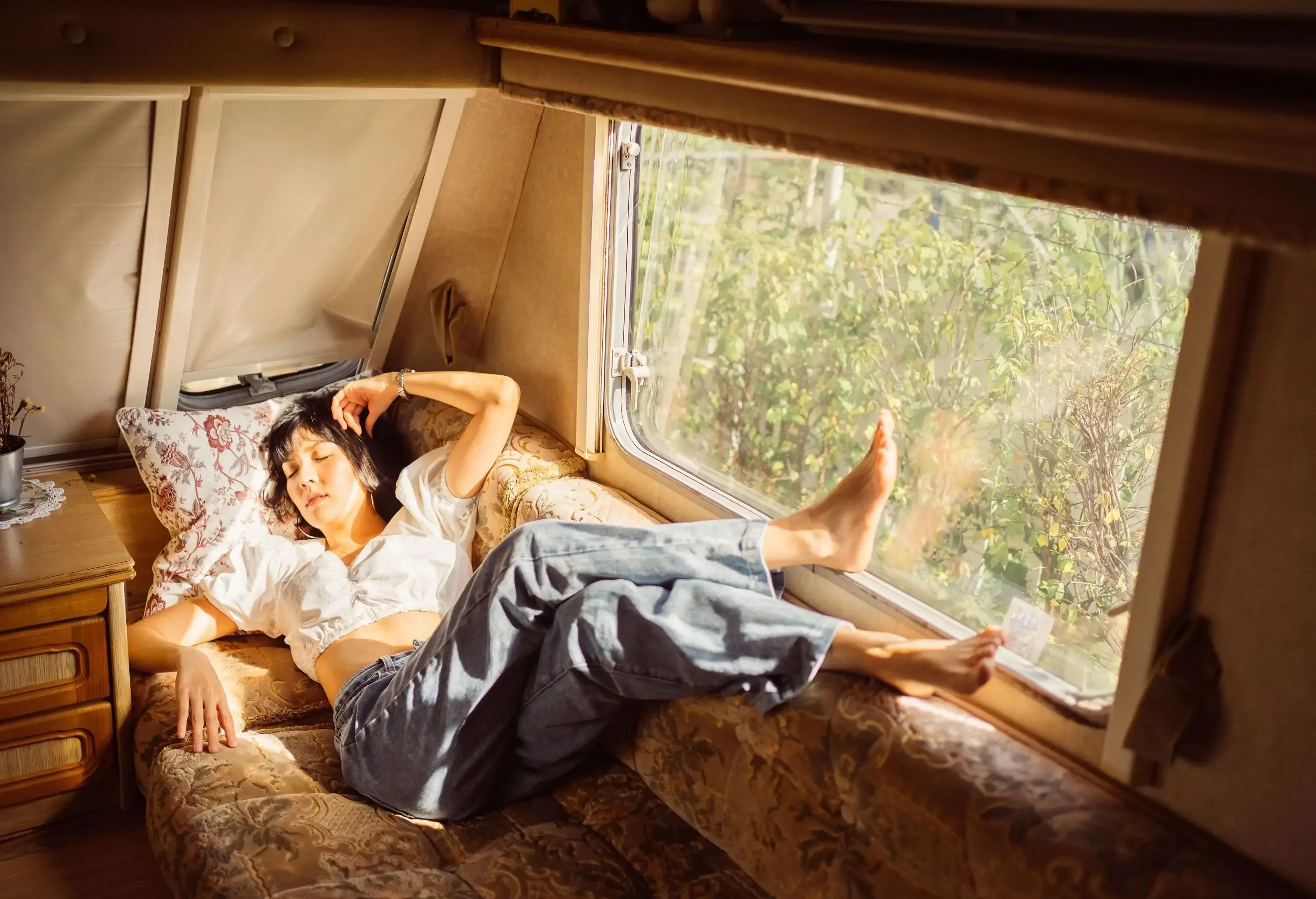 A woman dressed comfortably sleeps on a caravan sofa with her feet resting on the glass window.