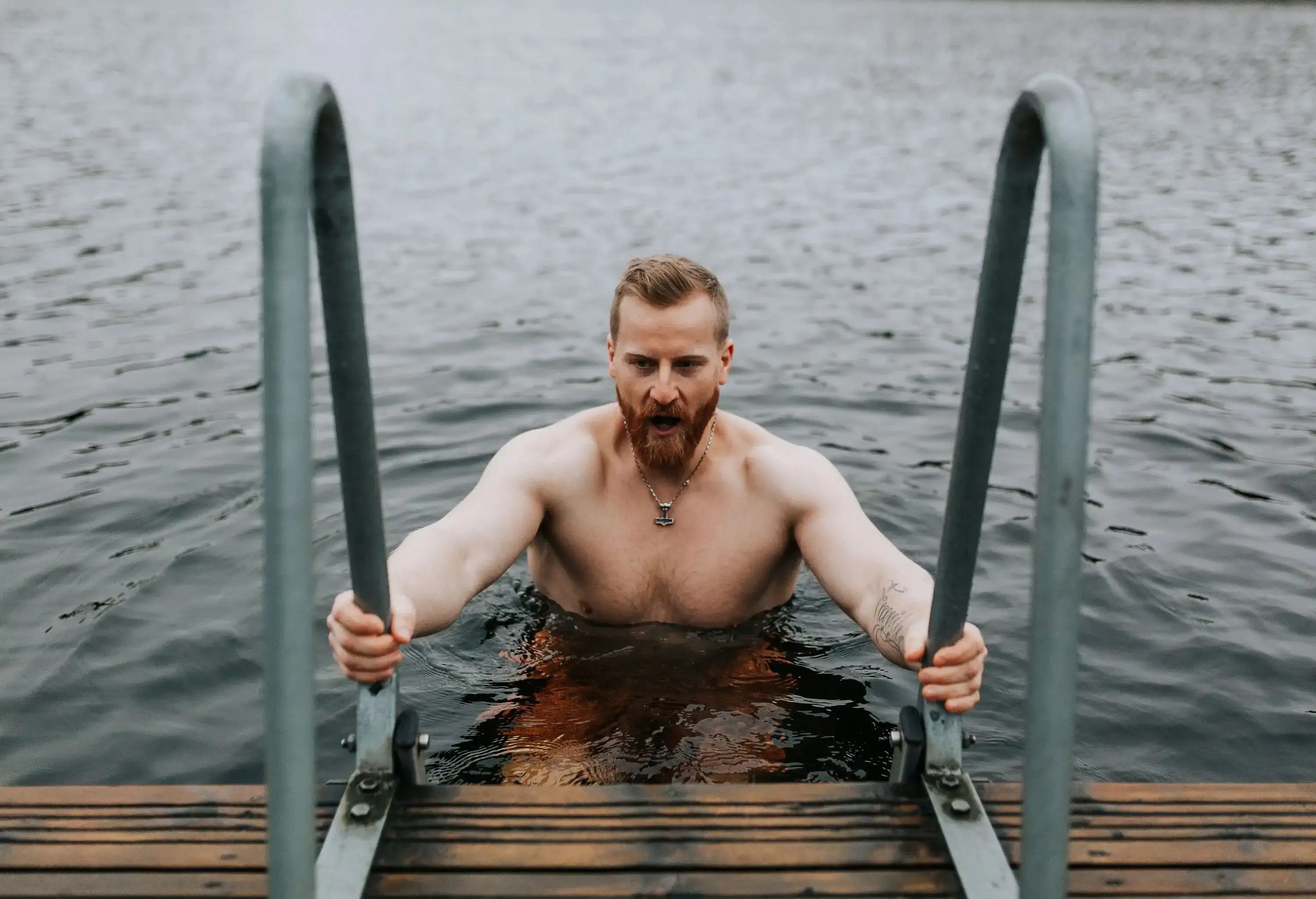 A man looking away while holding onto the rail, coming up from a swim in a cold lake.
